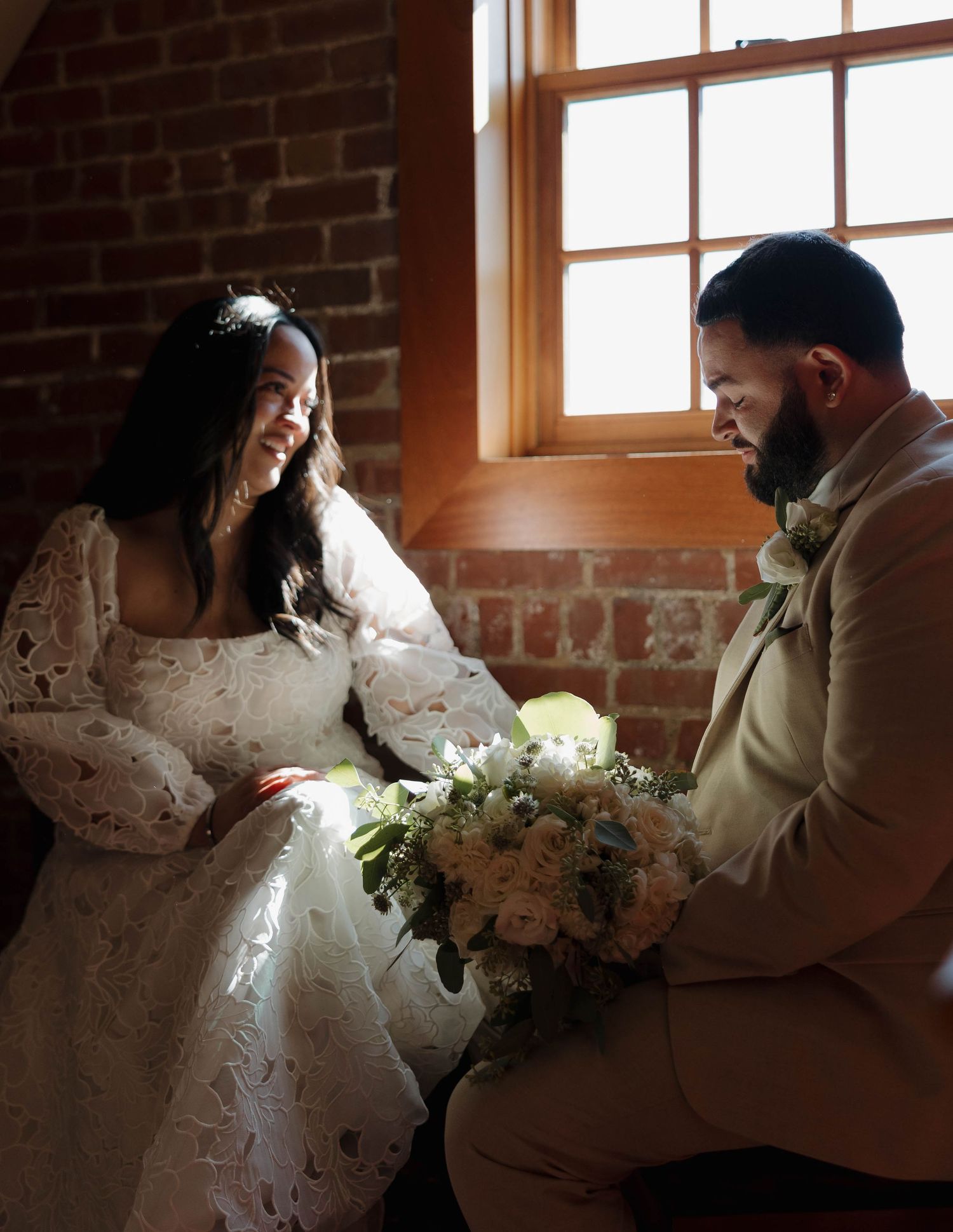 Intimate wedding moment captured in sunlit brick room with wooden floors.