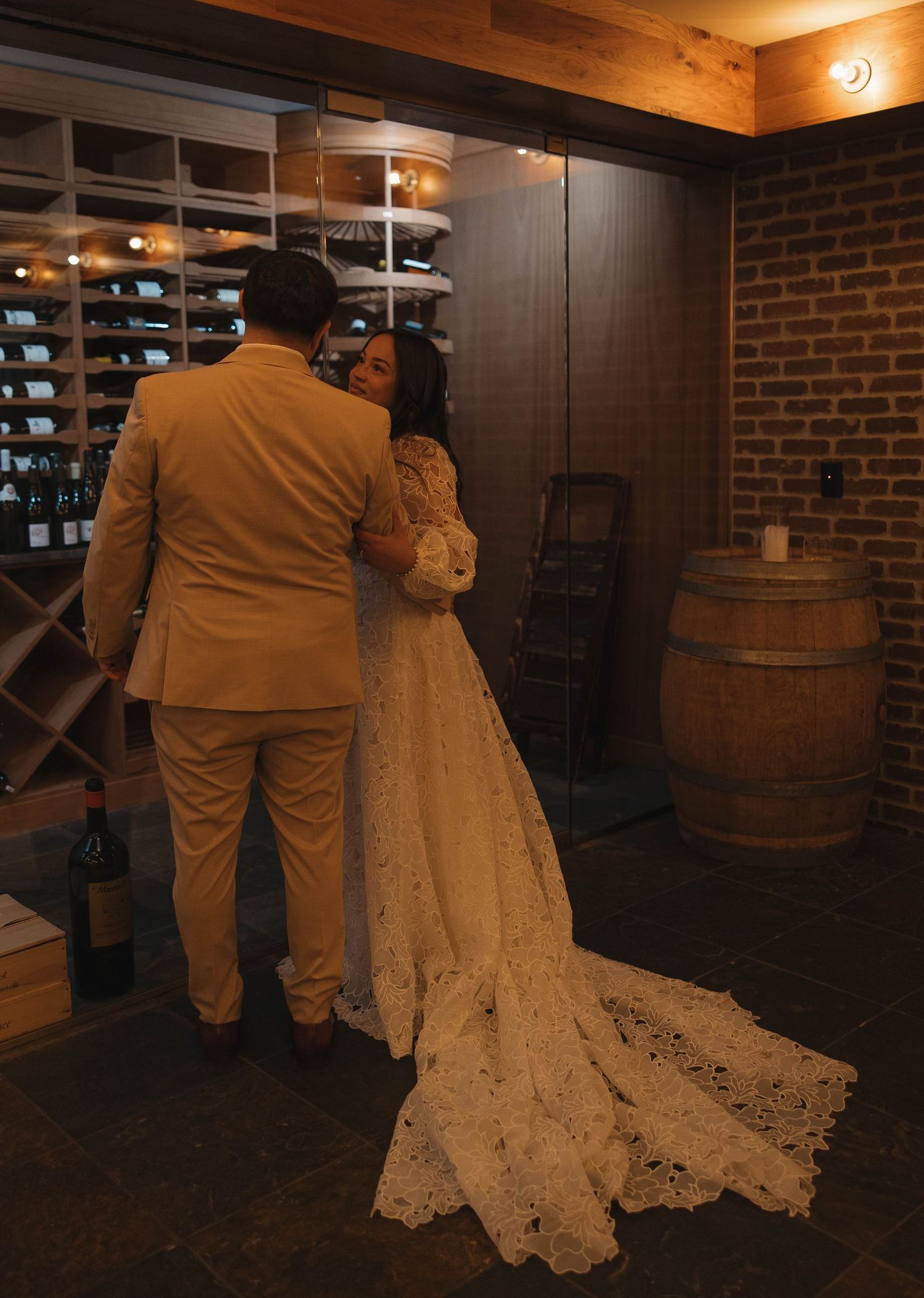 A couple dances in a rustic indoor venue with exposed brick walls and wooden barrels.