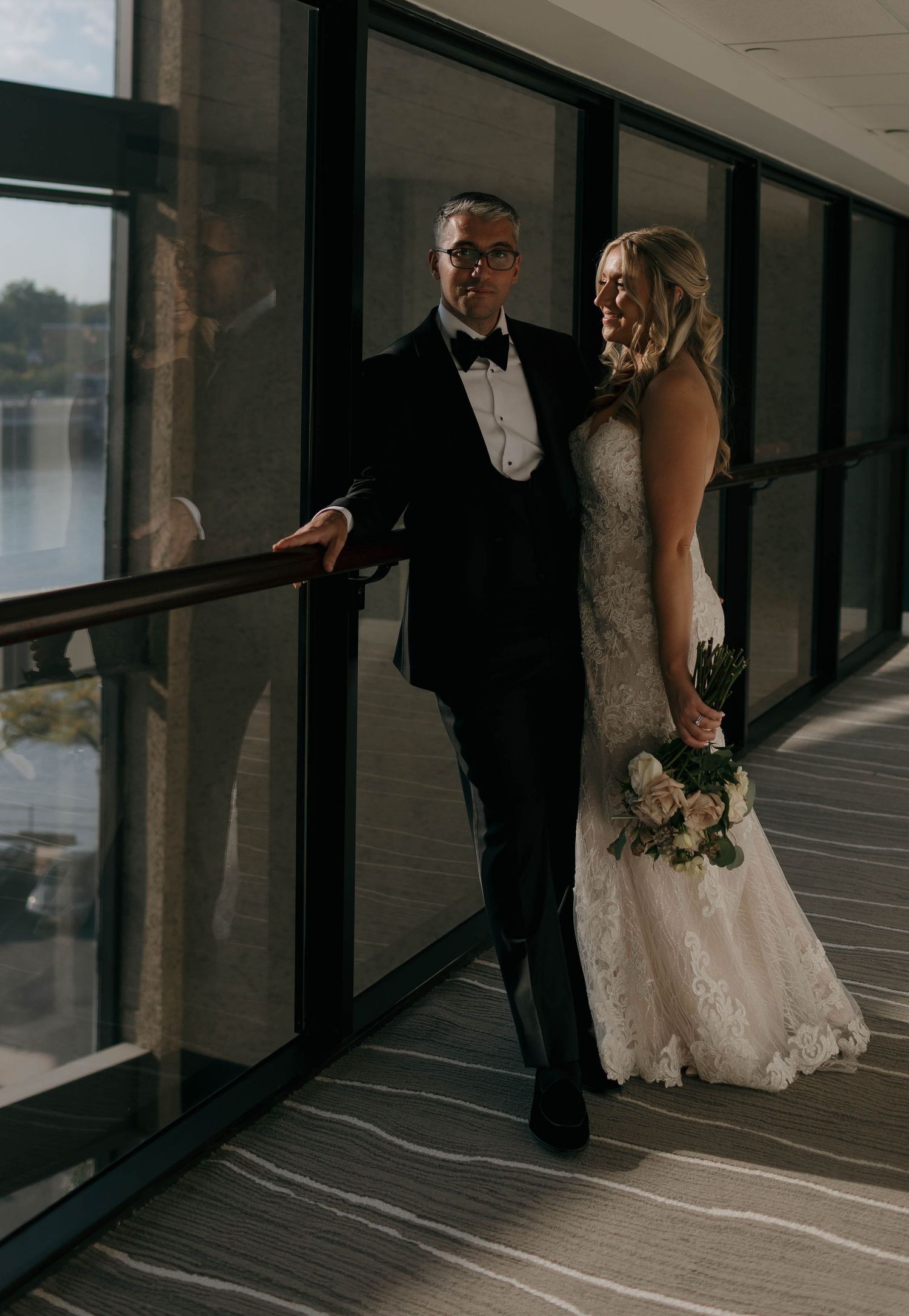 Wedding couple shares intimate moments in a modern hallway with window lighting.