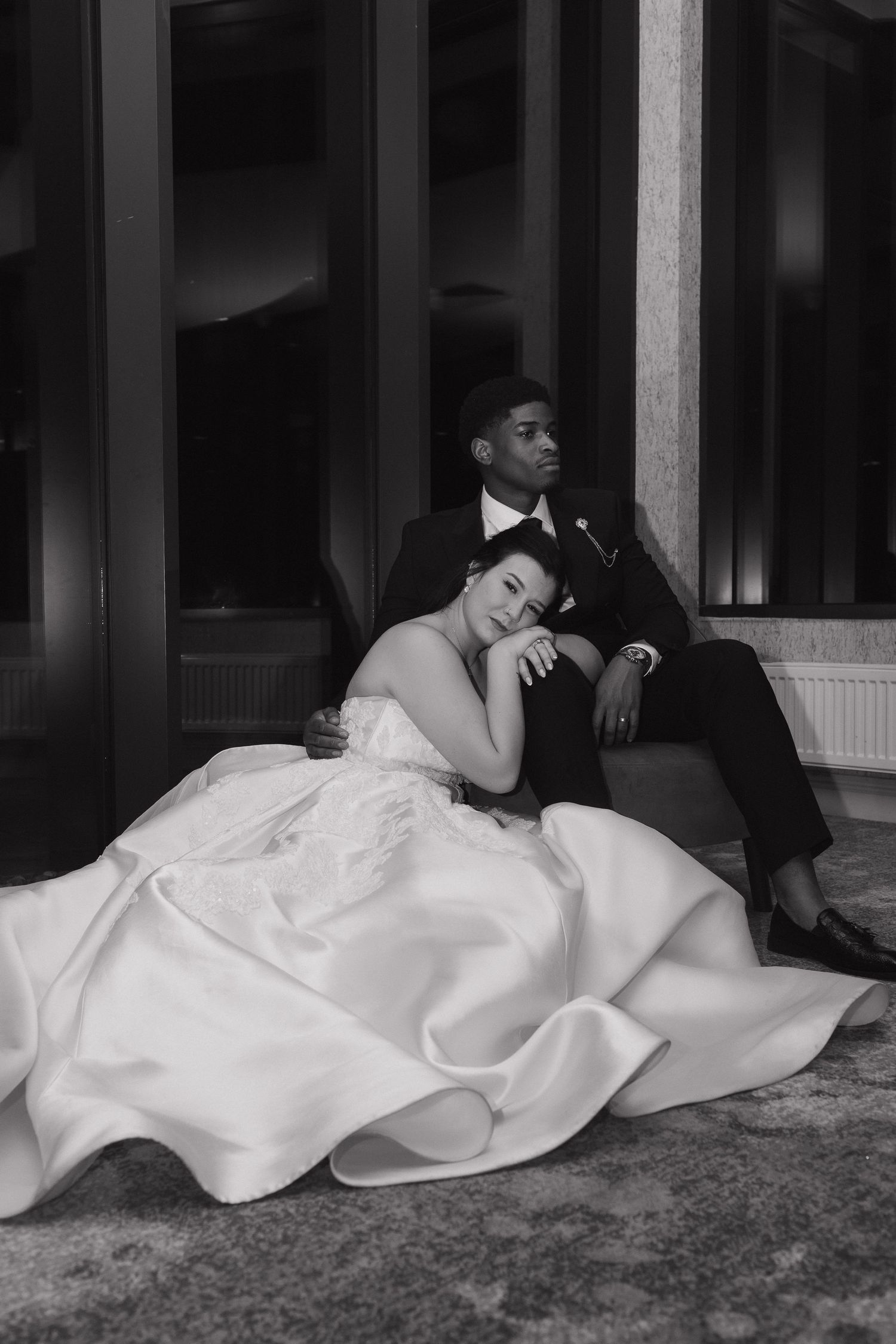 A black and white photo series shows two people lying down in formal wedding attire on a carpeted floor.