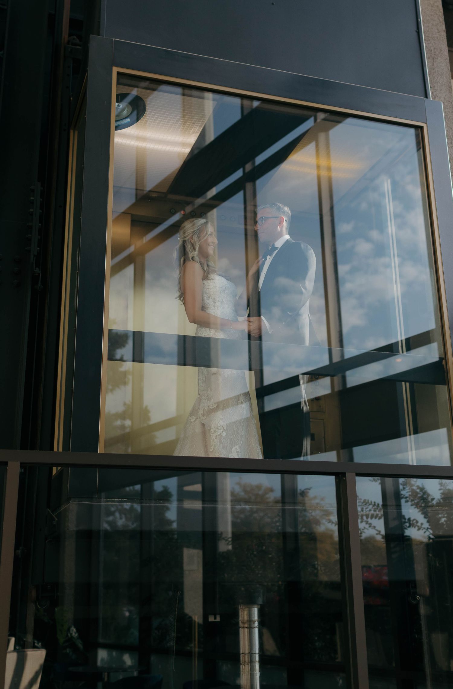 Reflective glass elevator exterior showing elegant wedding couple silhouettes.