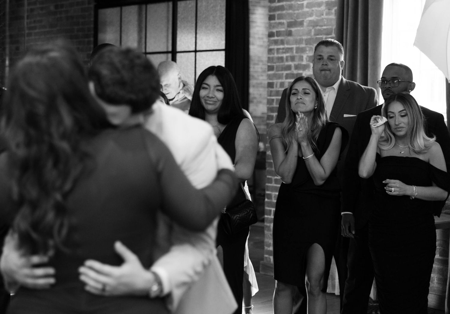 Wedding guests watch as newlyweds share their first dance in a brick-walled reception venue.