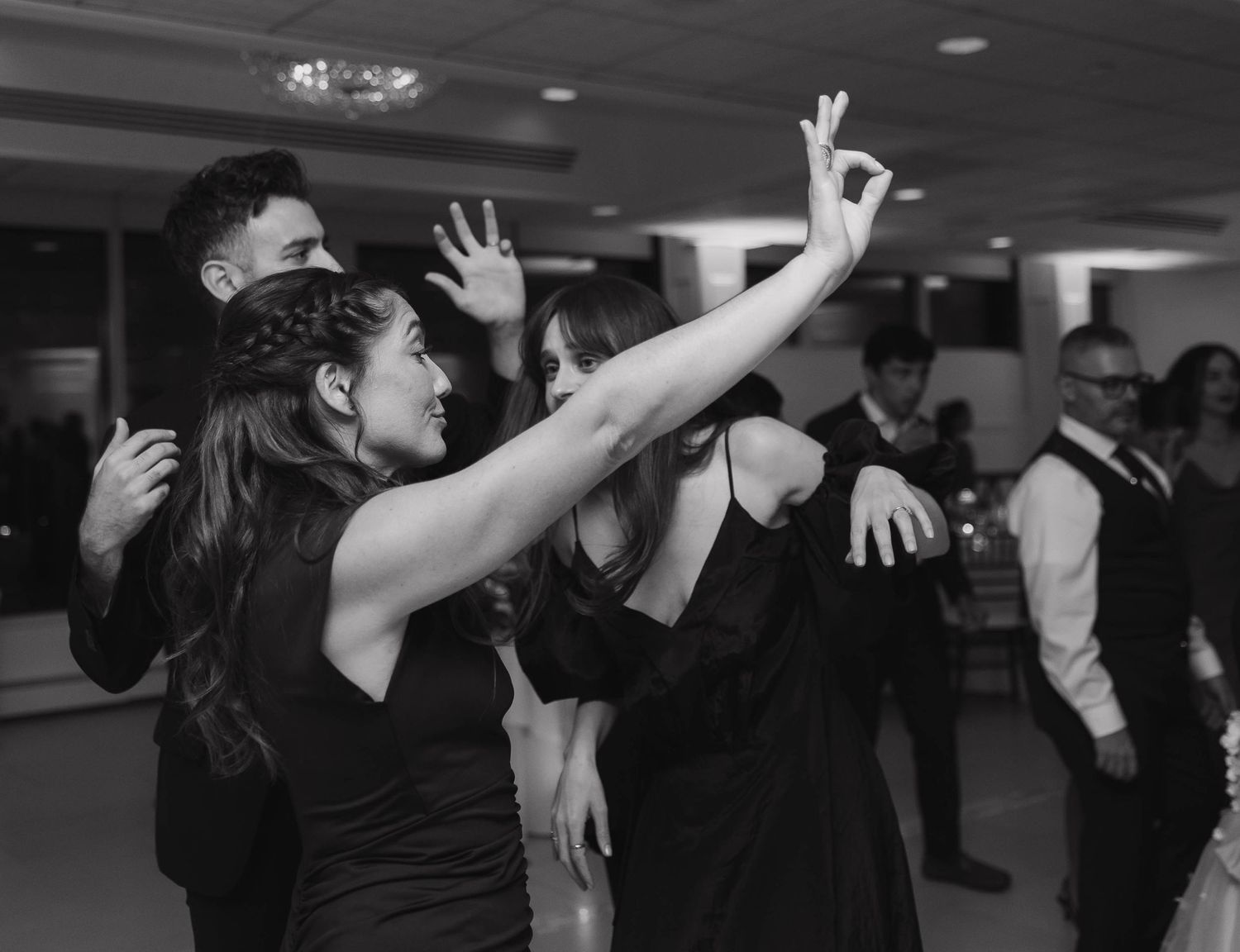 Wedding guests dancing and raising hands on dance floor at reception.