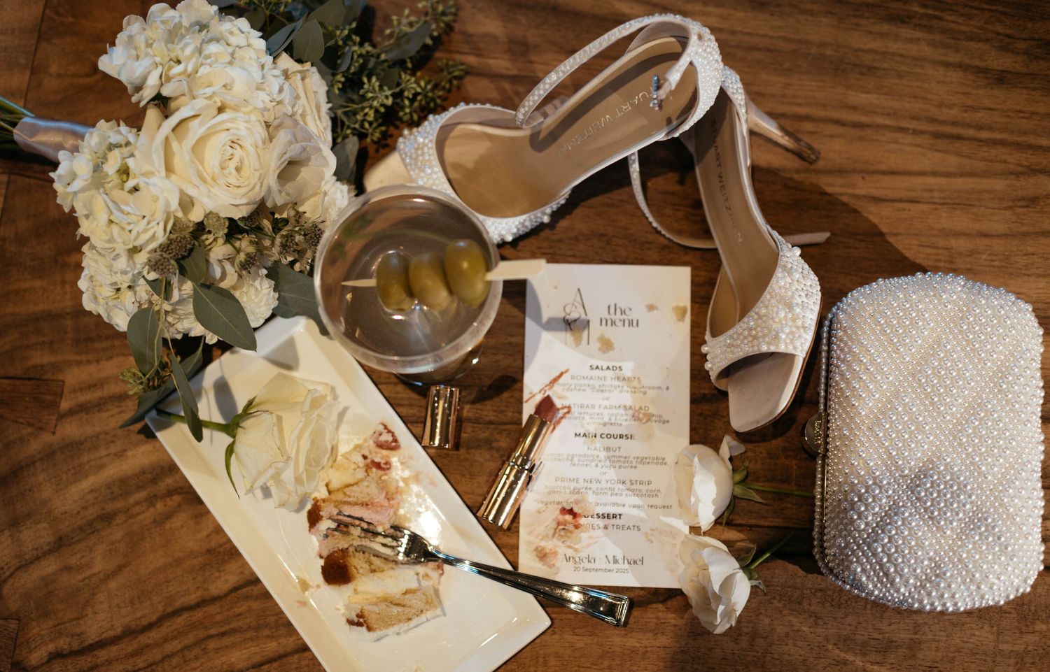 Wedding reception details with white roses, greenery, and paper goods arranged on wooden surface.