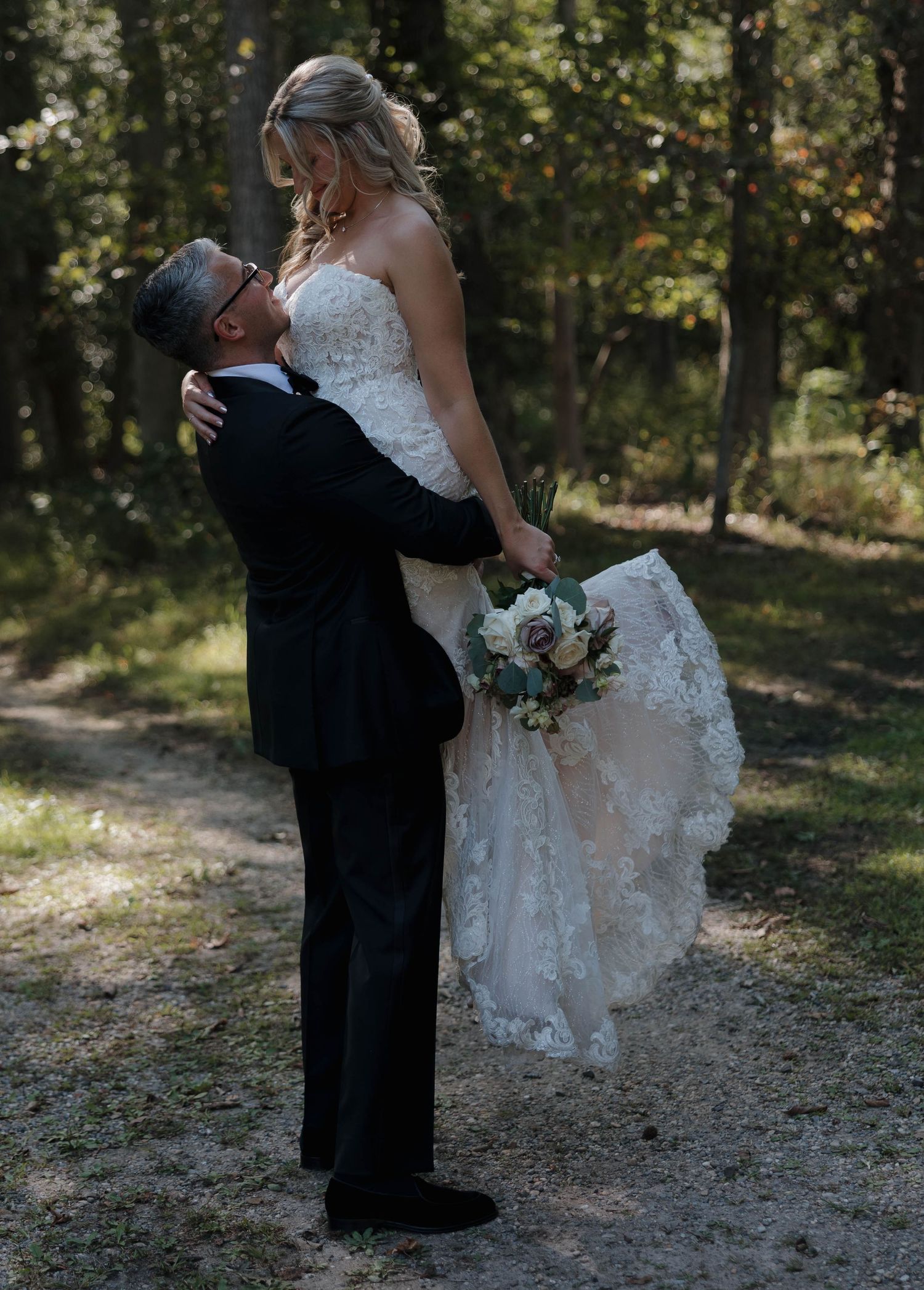 A couple embraces outdoors during their wedding photoshoot in a wooded setting.