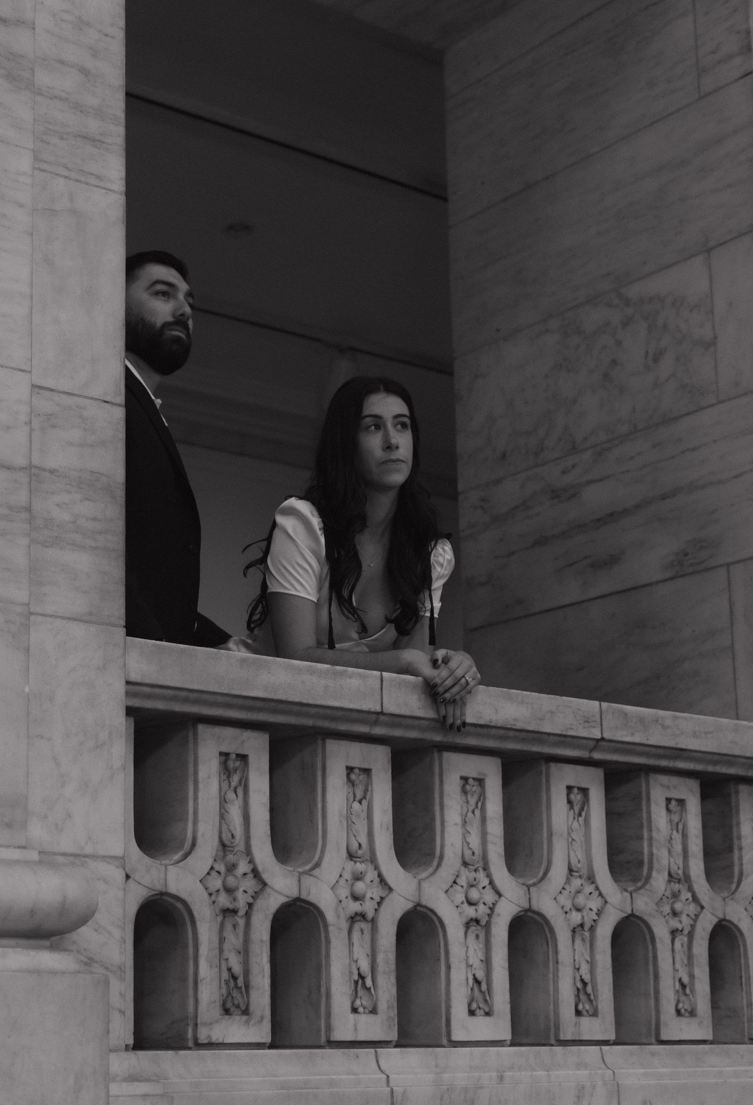 Two people lean against an ornate marble balustrade in a historic building.