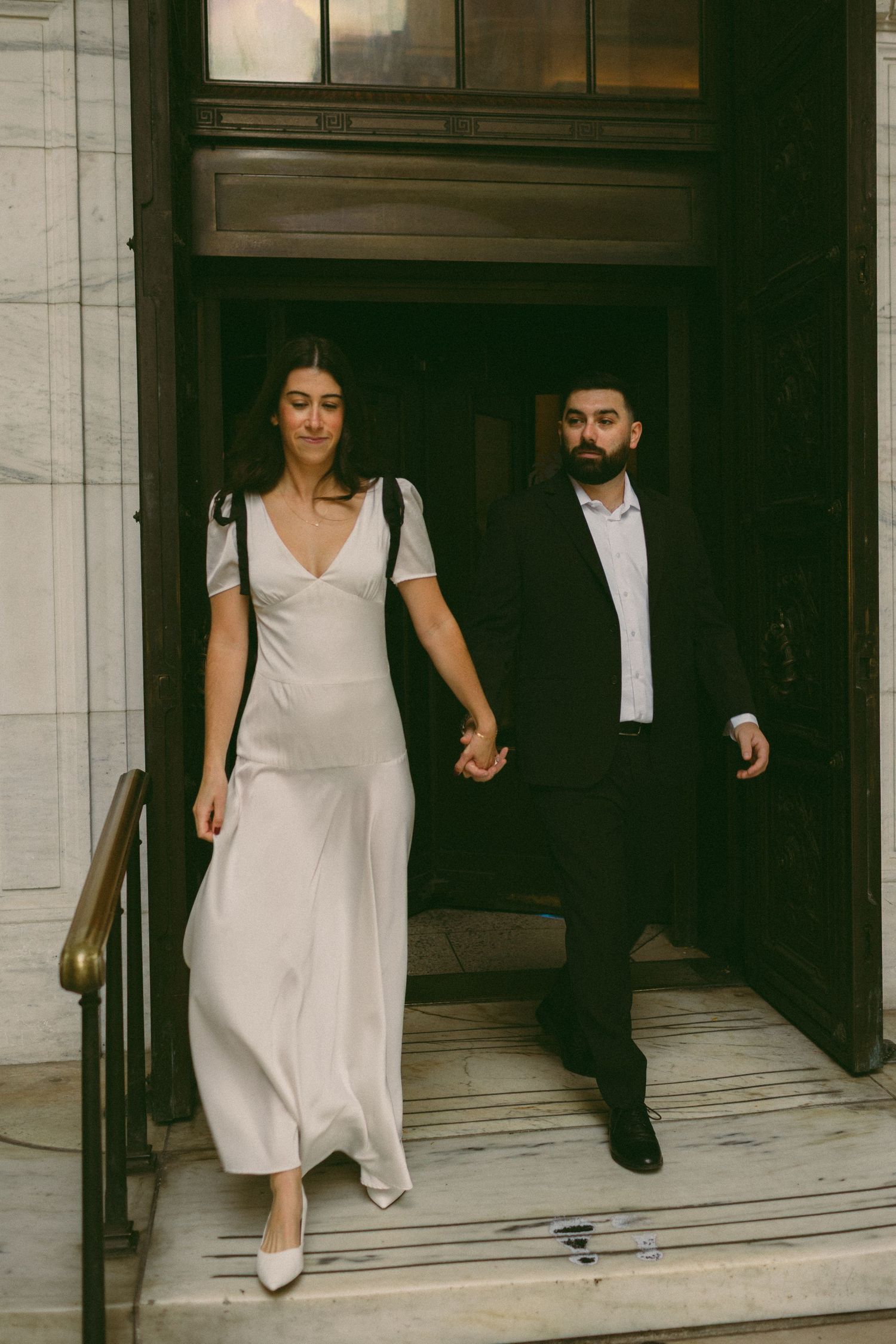 A couple exits through an ornate doorway, with the woman in white and man in black formal wear.