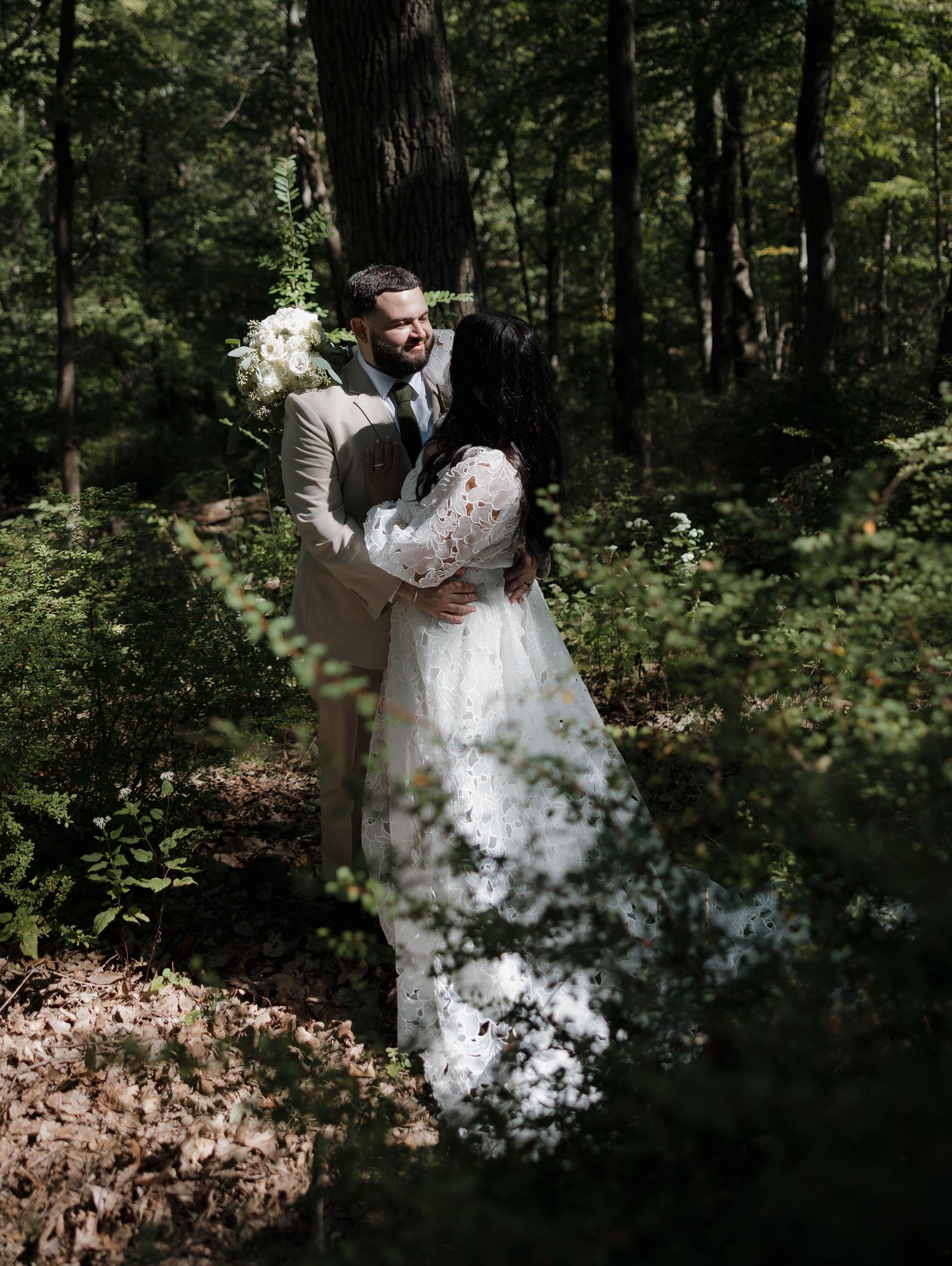 A couple dances together in a sunlit forest setting, the bride's white dress flowing elegantly through the scene.