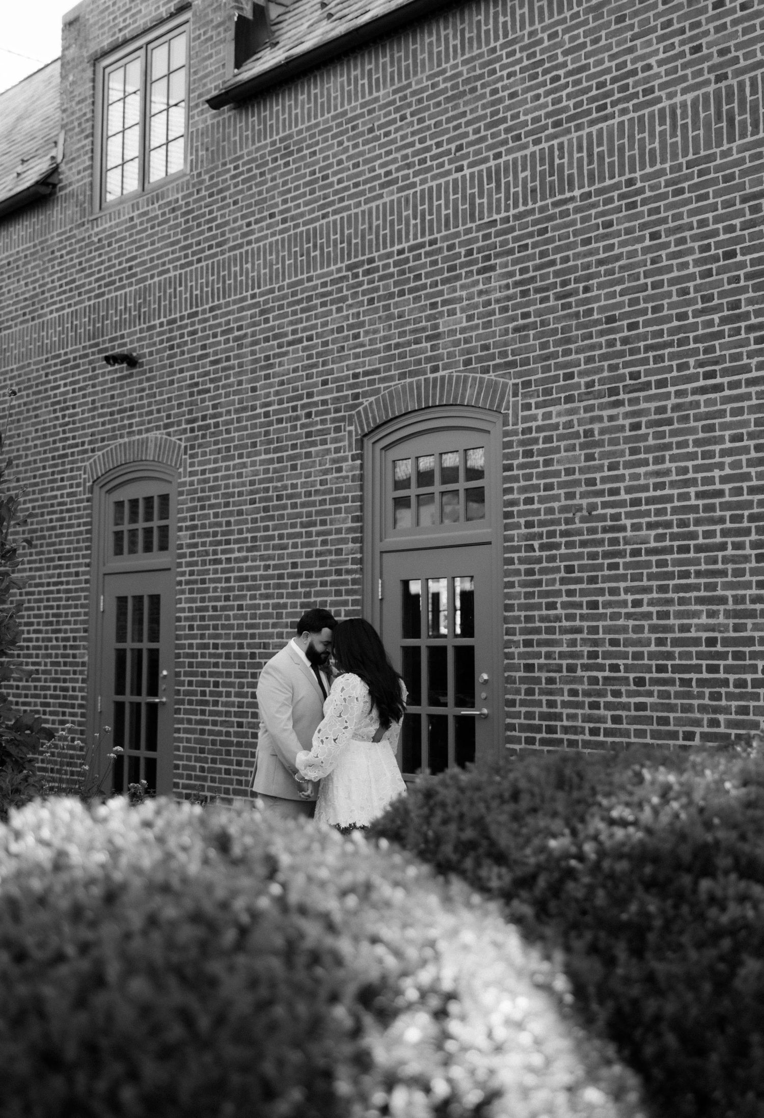 Black and white wedding photo with brick building and window details in background.