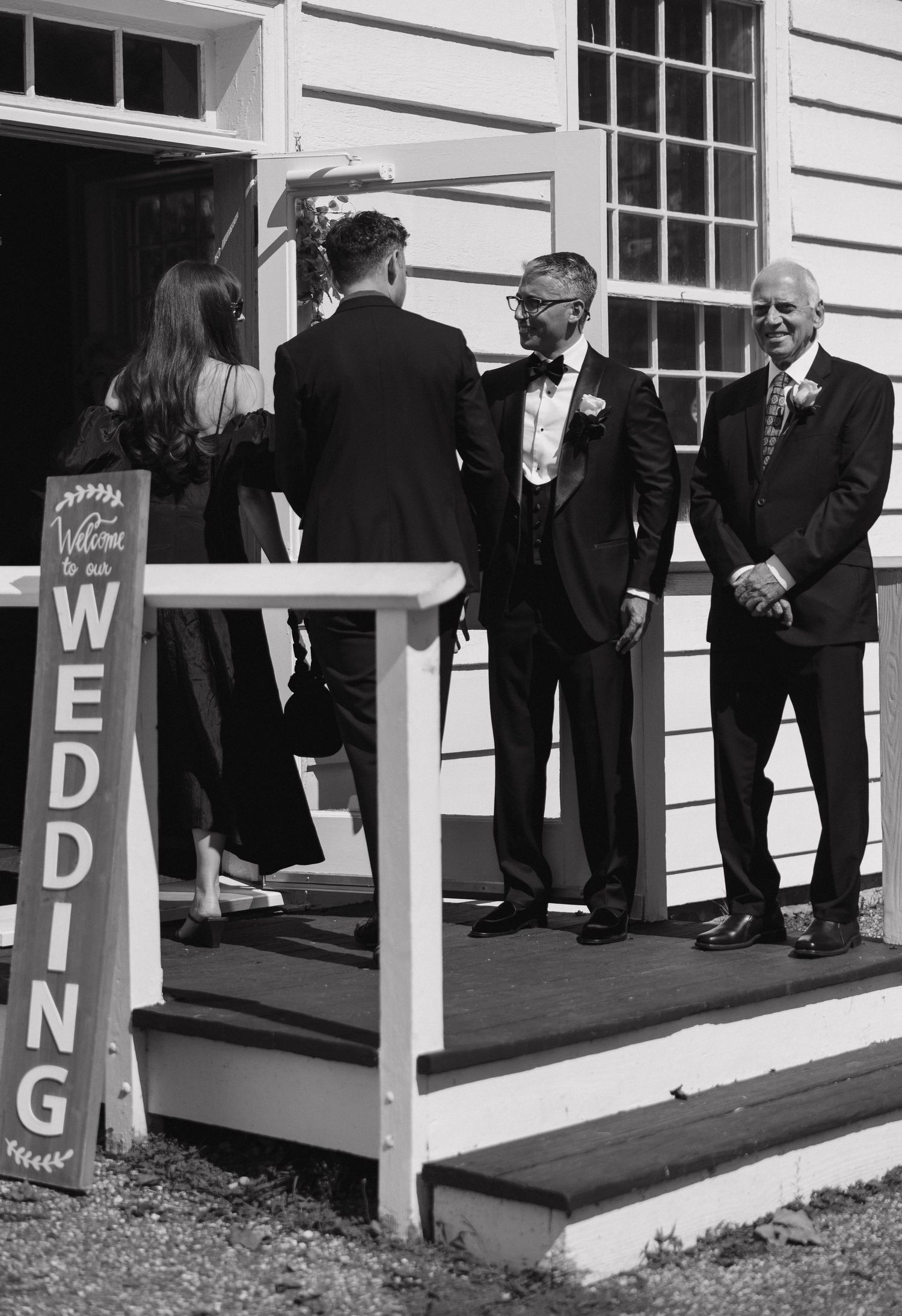 Wedding guests gather on a white porch with decorative lettered signs.