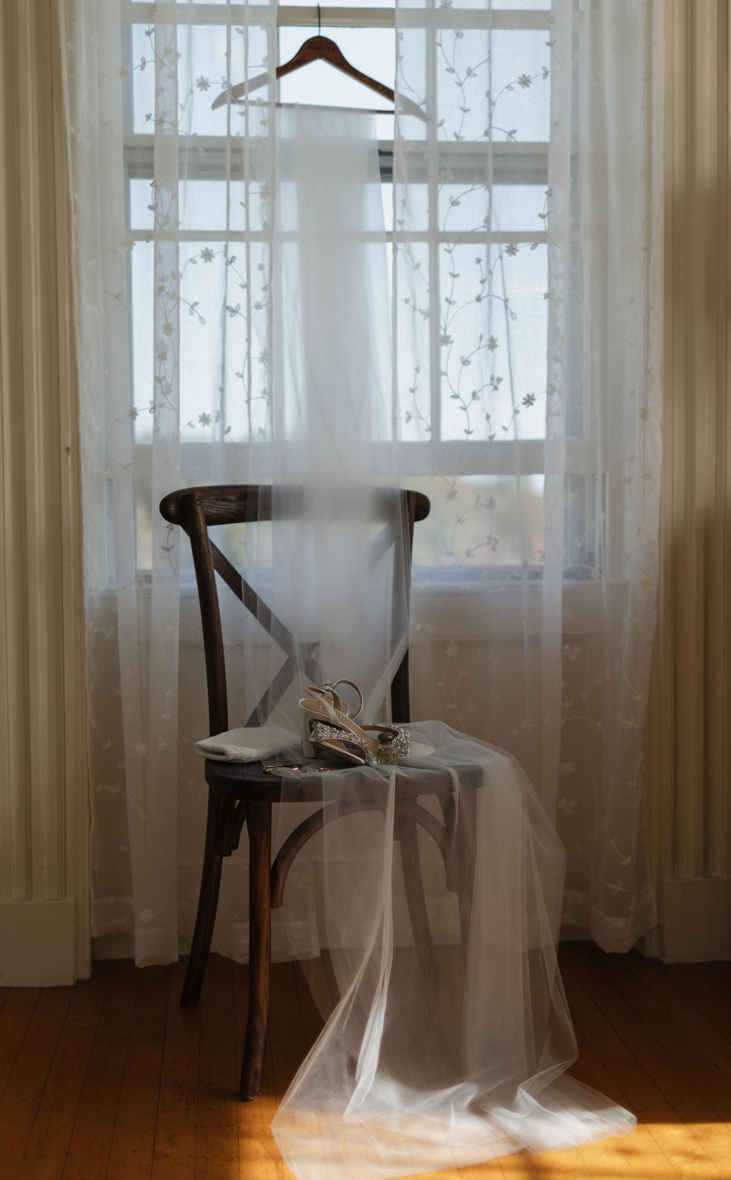 Ethereal bridal veil hanging in sunlit room with sheer curtains and wooden chair.