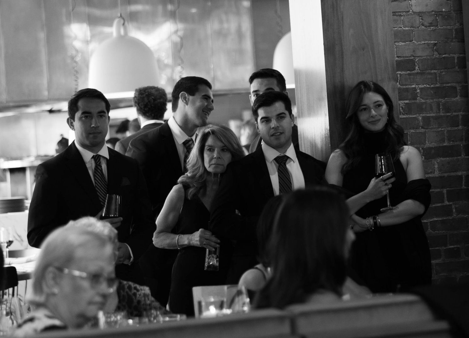 A black and white candid shot of wedding guests mingling at a reception.
