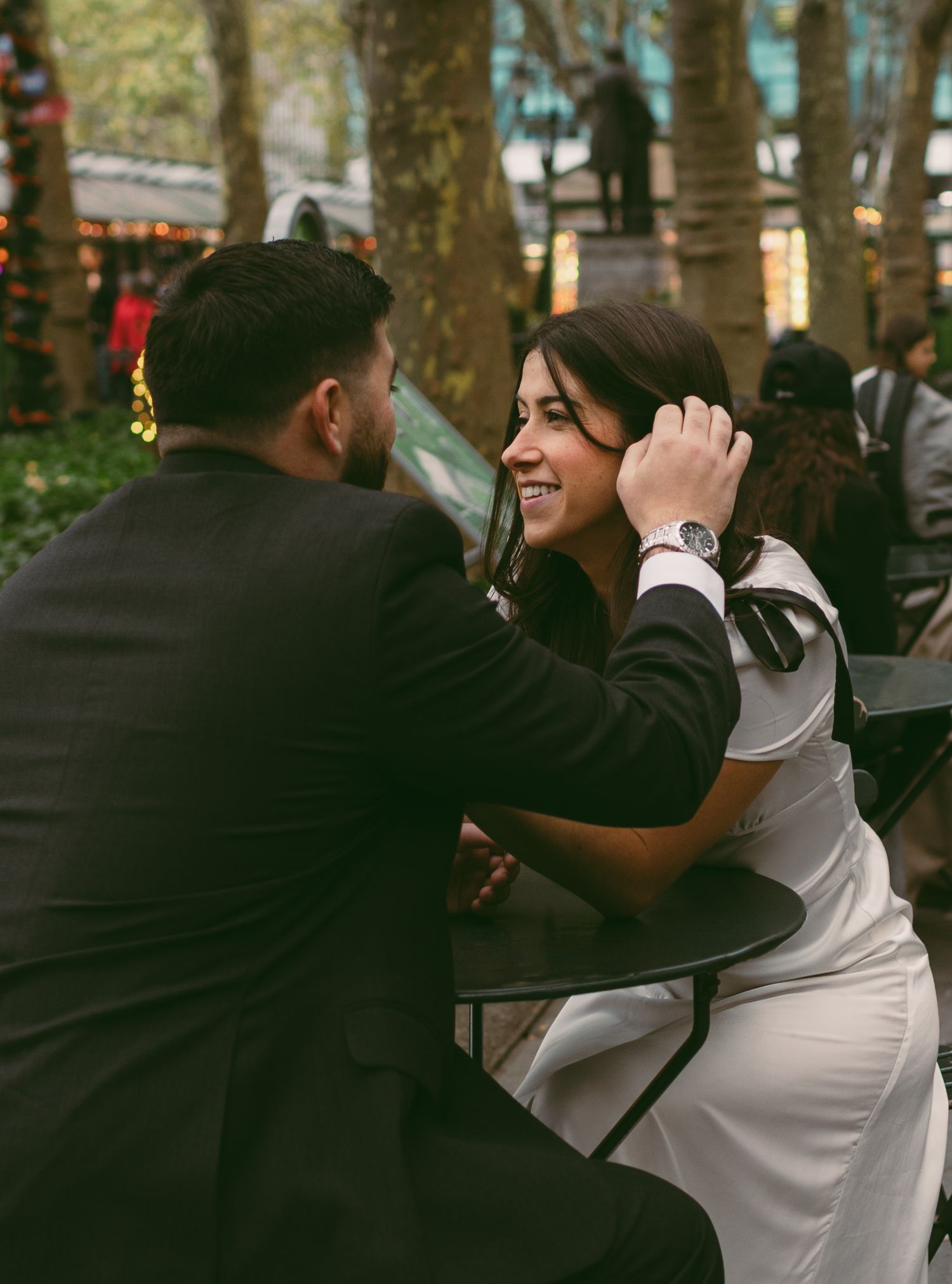 A couple sharing a tender moment in a park setting with trees in the background.