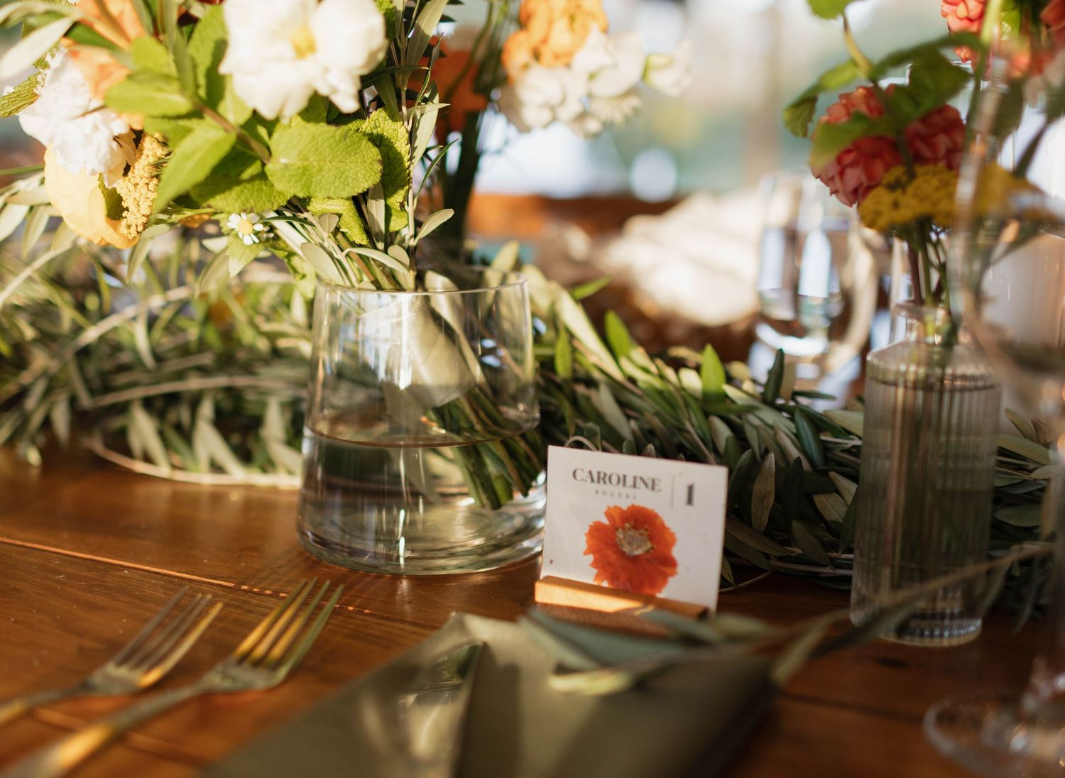 Wedding table setting with floral centerpieces in glass vases and name cards.