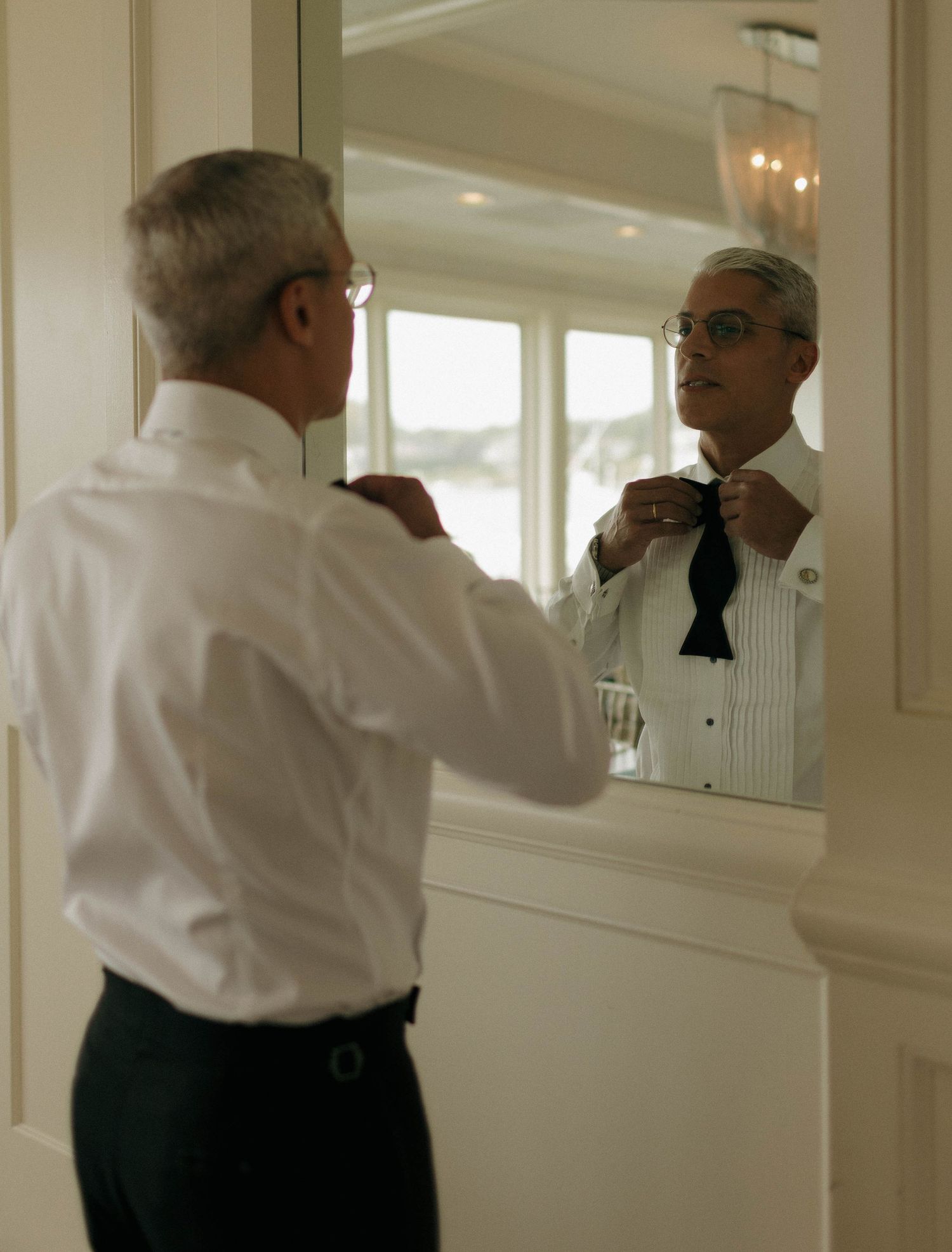 People in formal wear adjusting their attire in front of a mirror.