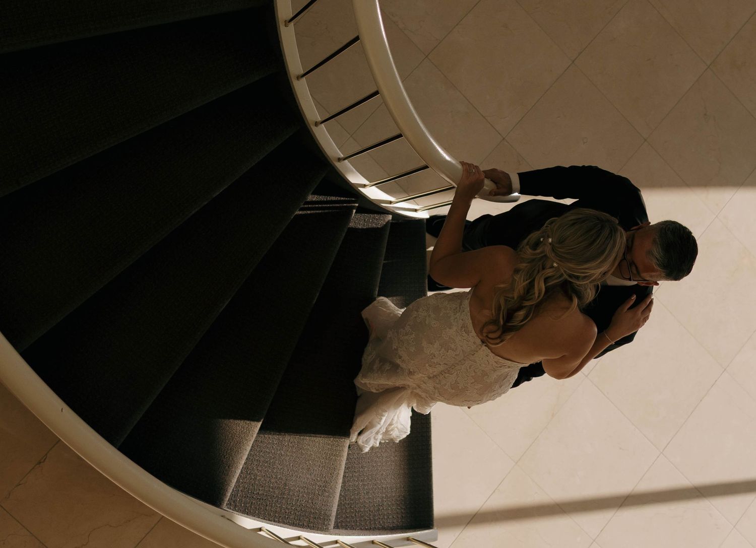 Aerial perspective of a couple on a dramatic spiral staircase during a wedding photoshoot.