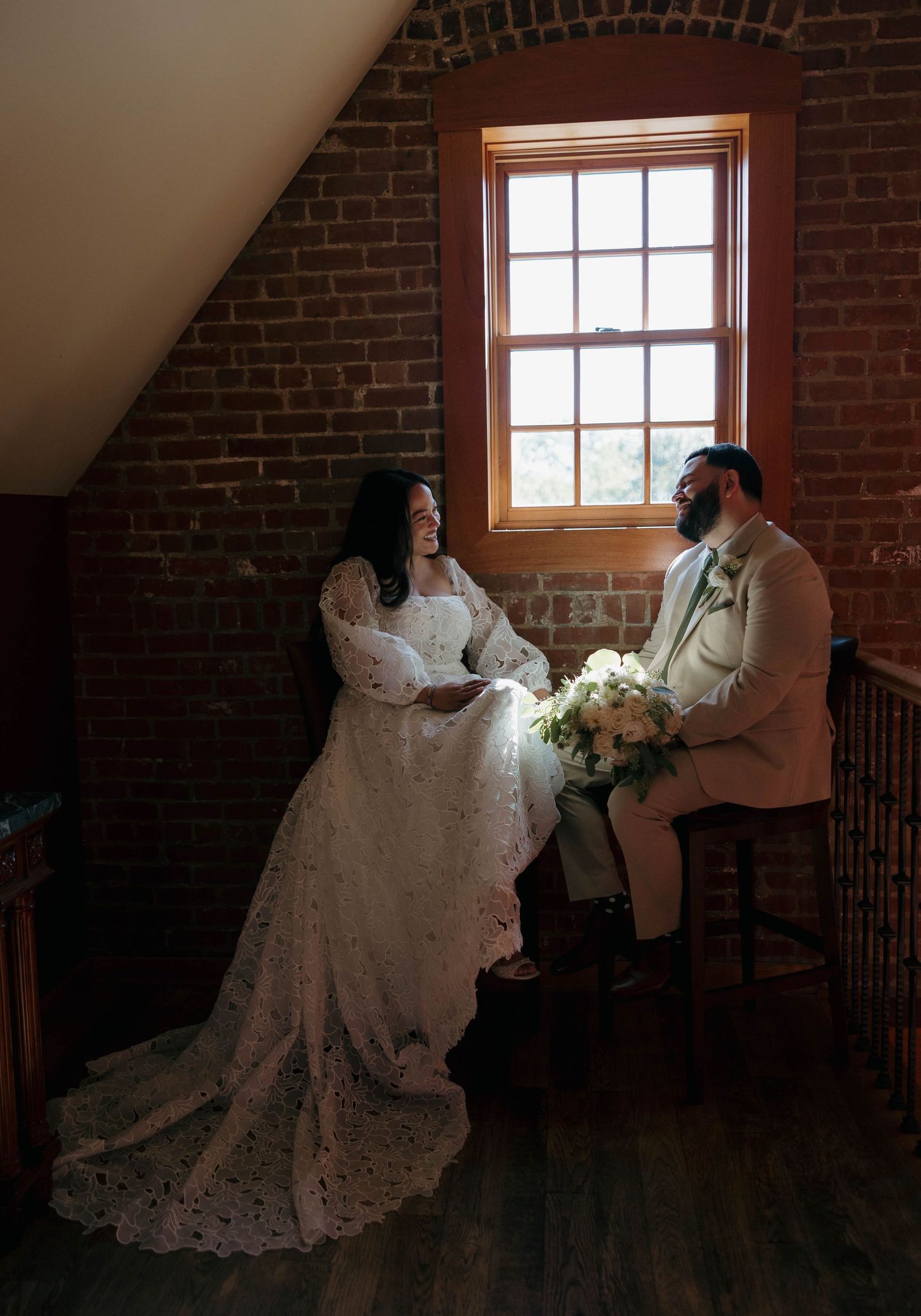 Wedding couple interacts in vintage brick room with beautiful natural window lighting.