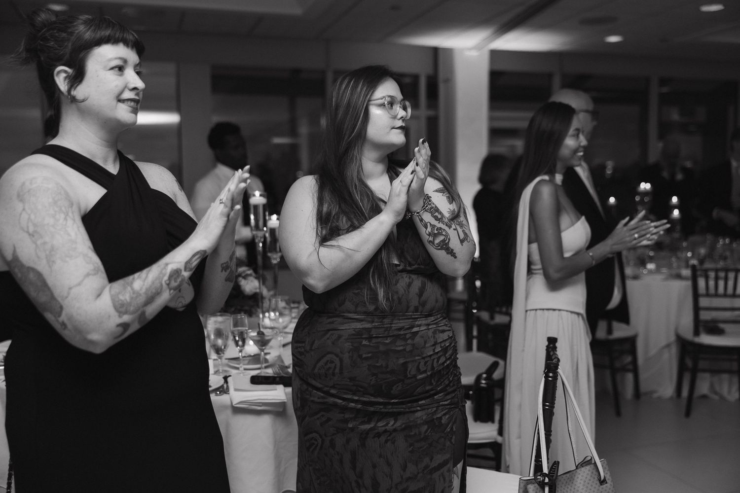Wedding guests in formal attire singing or cheering at reception.