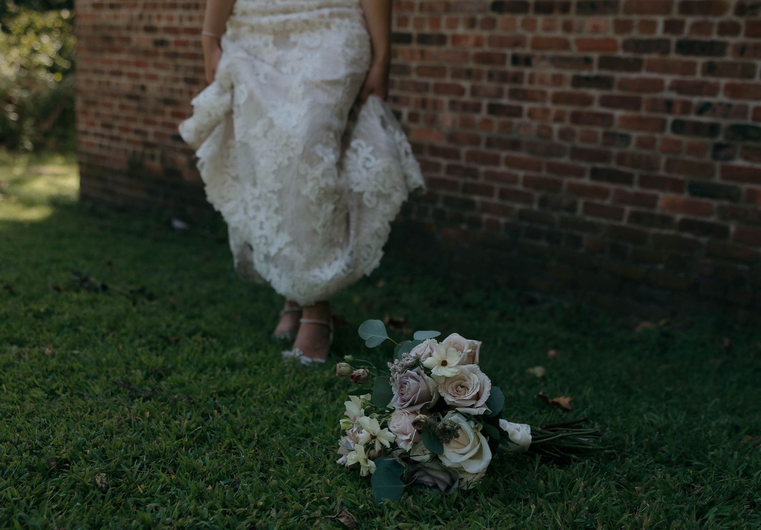 White wedding bouquet lies on grass next to flowing lace dress hem.