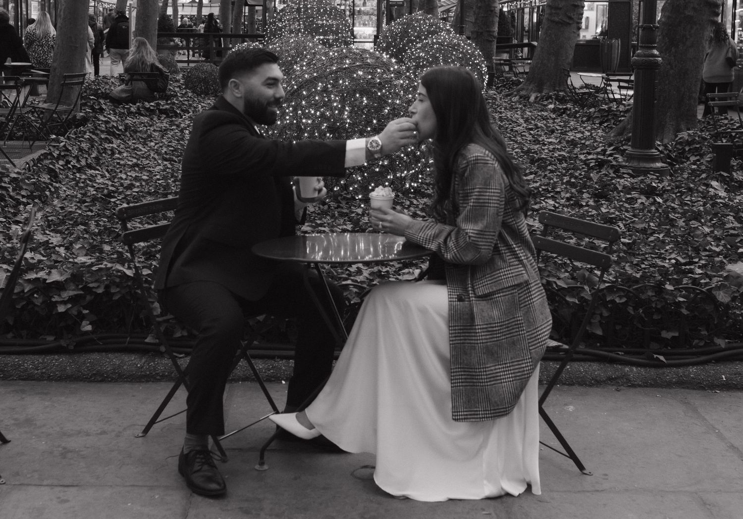 A couple shares a moment at an outdoor cafe table in black and white.