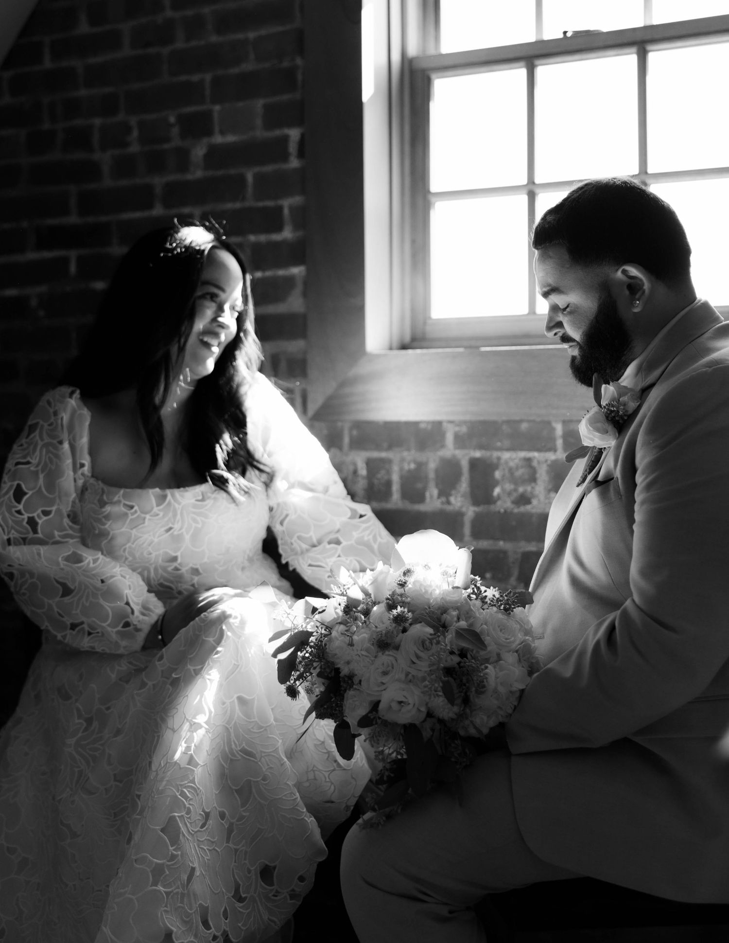 A romantic couple shares an intimate moment in a rustic brick room with natural window lighting.
