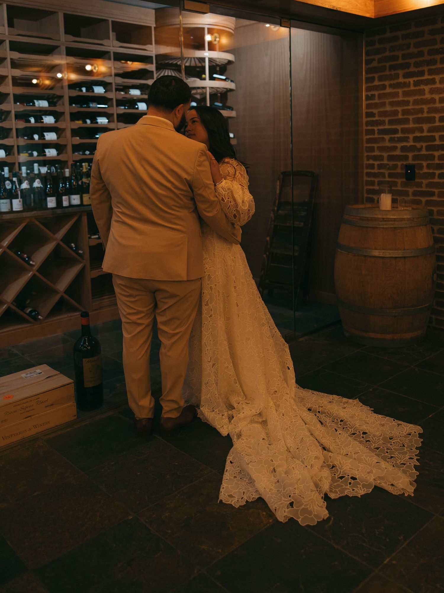 Couple shares an intimate moment in front of a wine rack at their wedding reception.