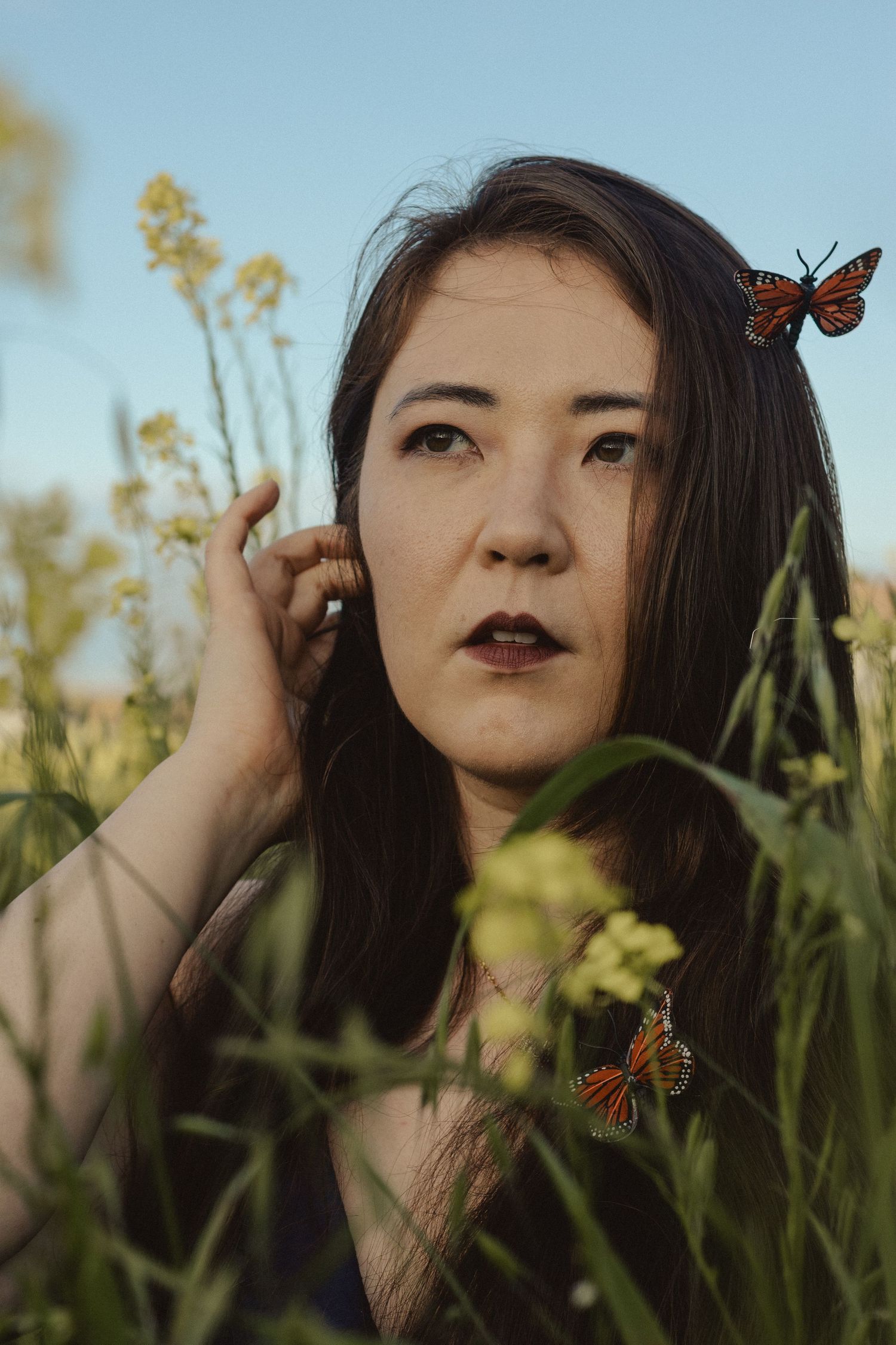 Artistic portrait with monarch butterflies against backdrop of yellow flowers and blue sky.