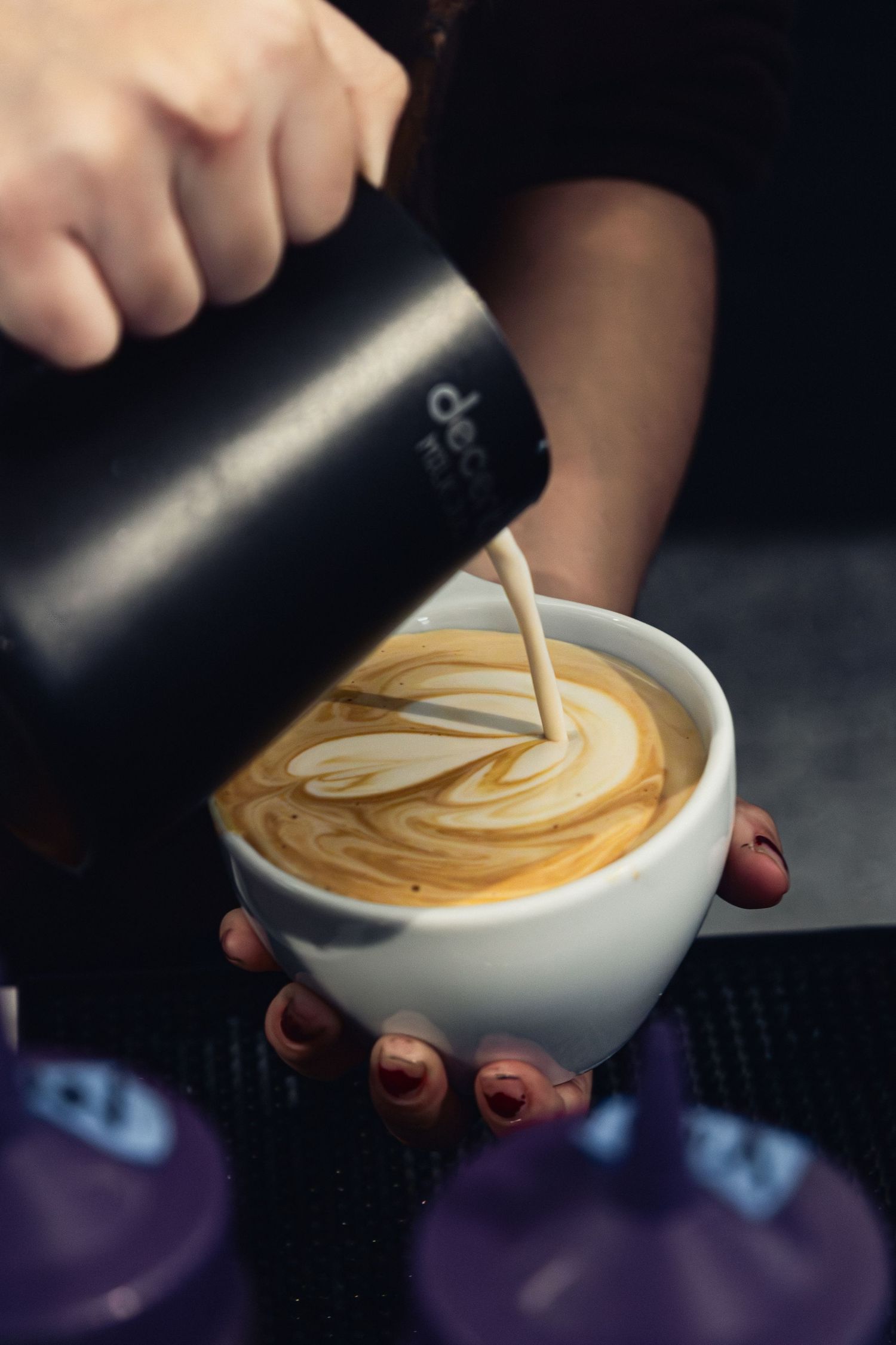 Close-up of latte art being created with steamed milk poured into a white ceramic cup.