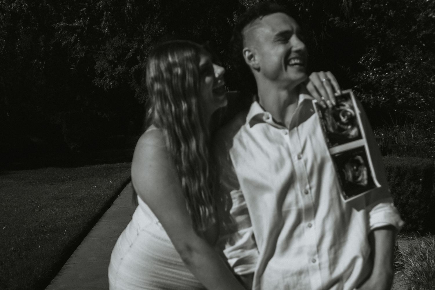 A couple sharing a joyful moment while holding ultrasound photos outdoors.