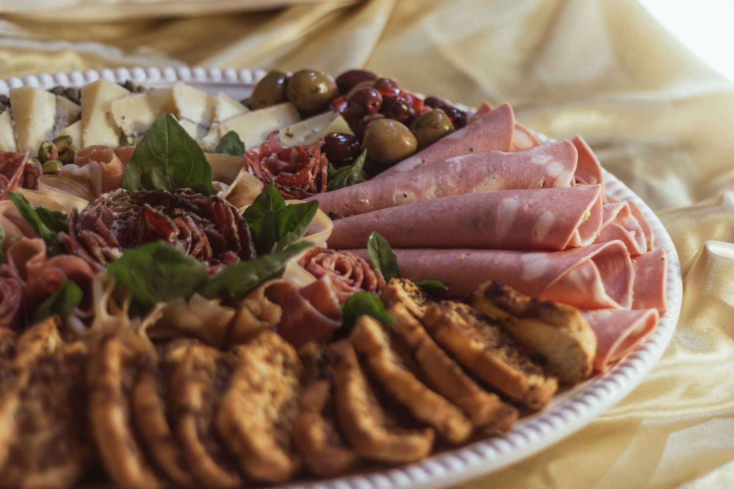 Elegant charcuterie platter with sliced ham, salami, olives, and garnishes on a white plate.
