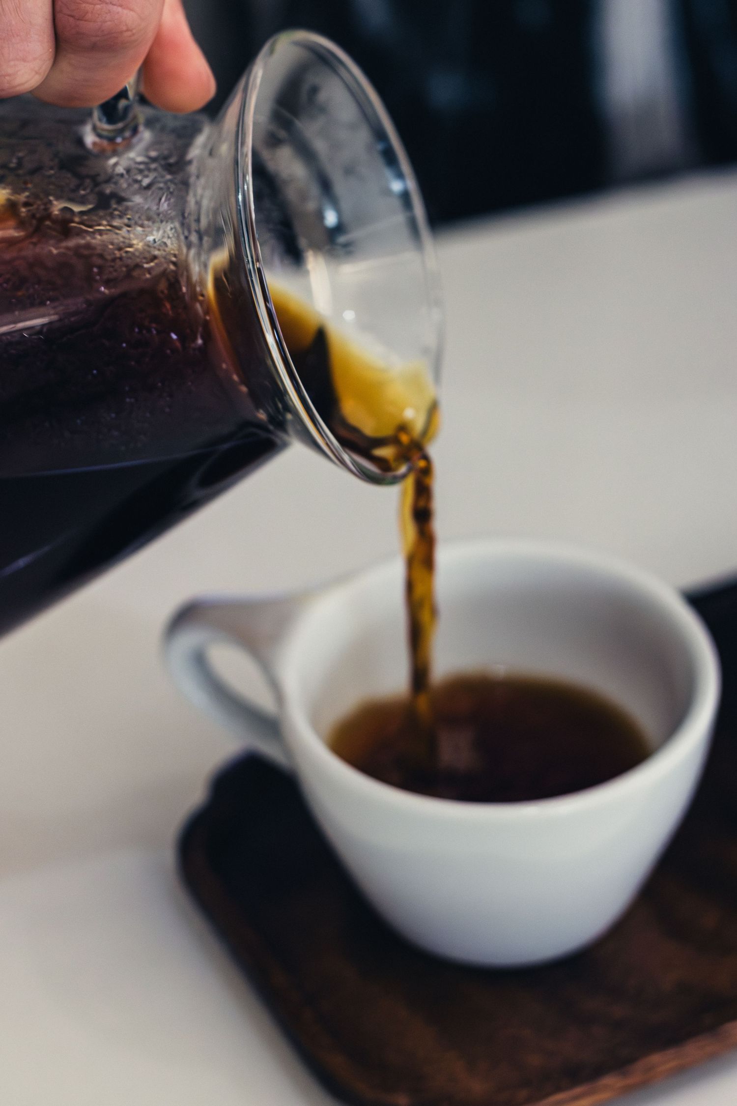 Coffee being poured from a glass carafe into a small white serving vessel.