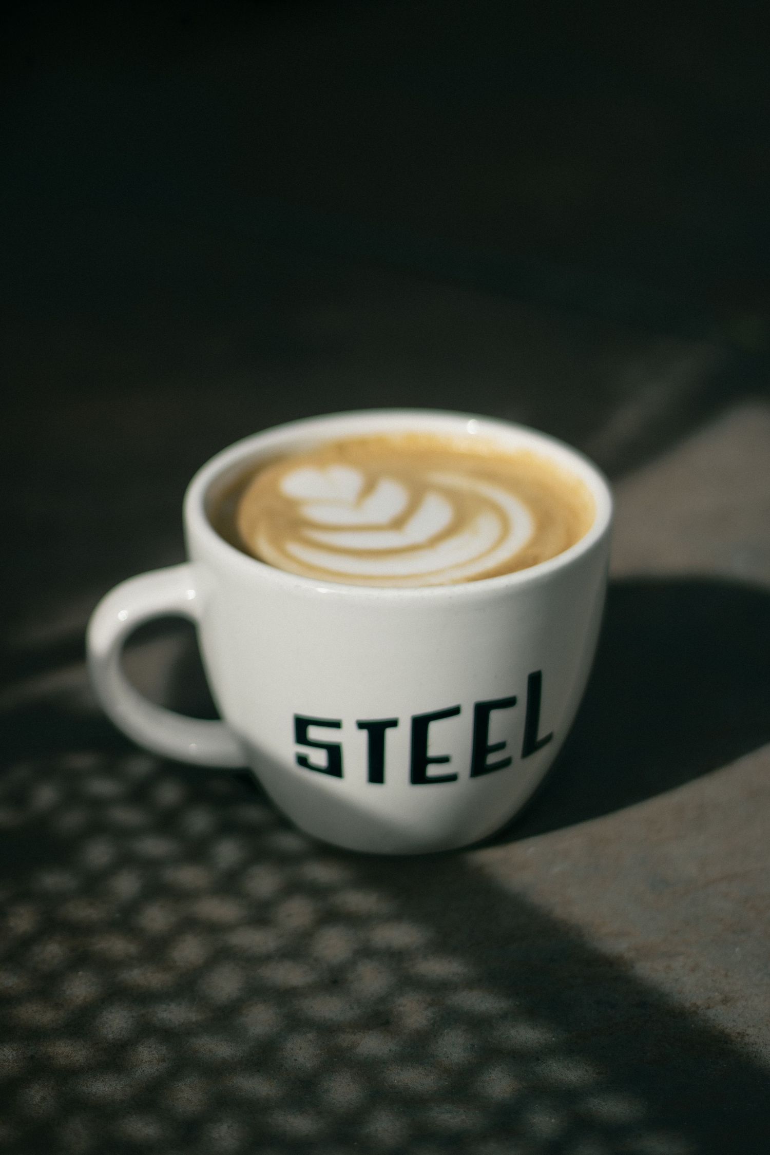 A series of white coffee cups with latte art showing a progression of the same drink from different angles on a dark surface.