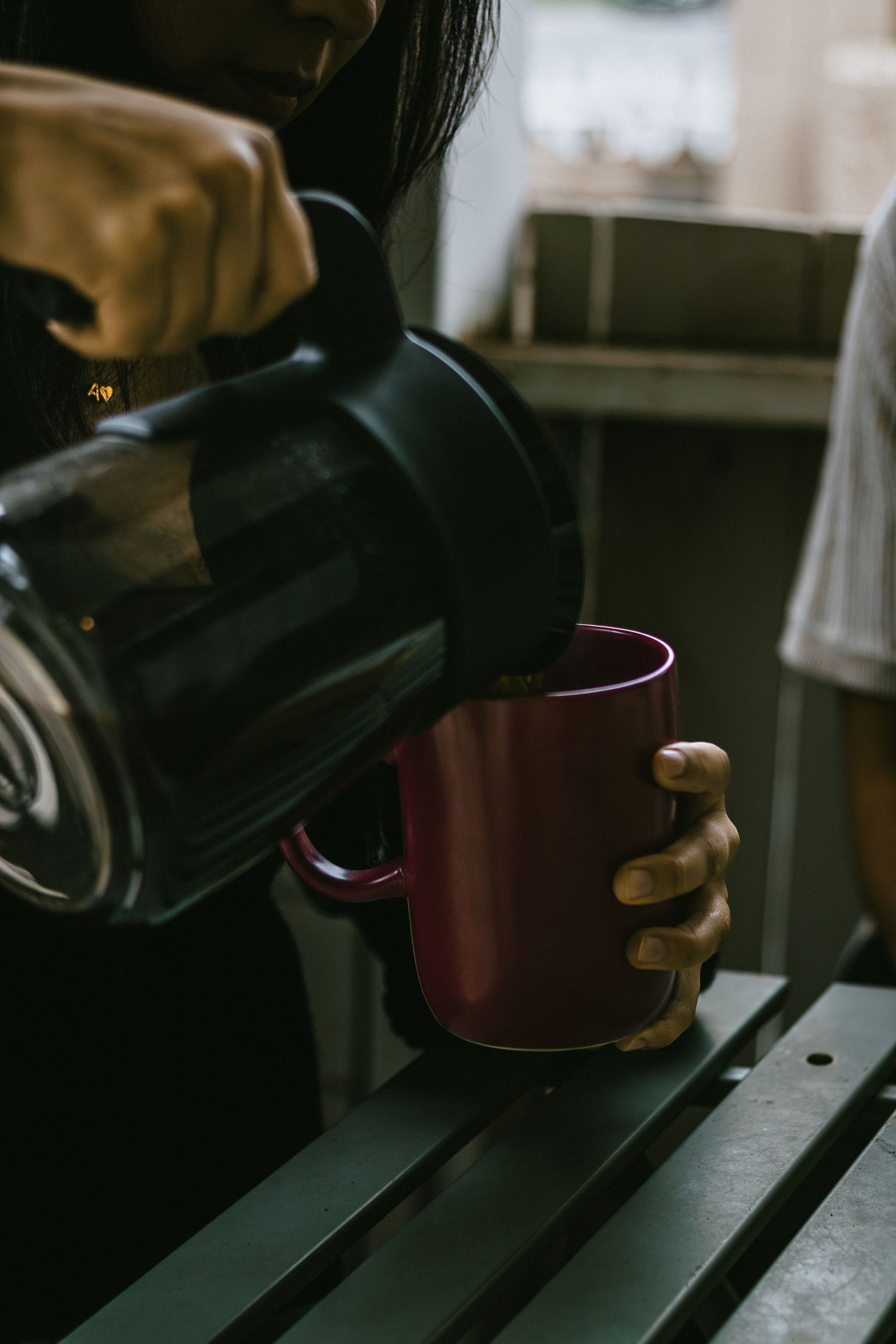 Close-up of hands holding a burgundy coffee mug on a dark surface.