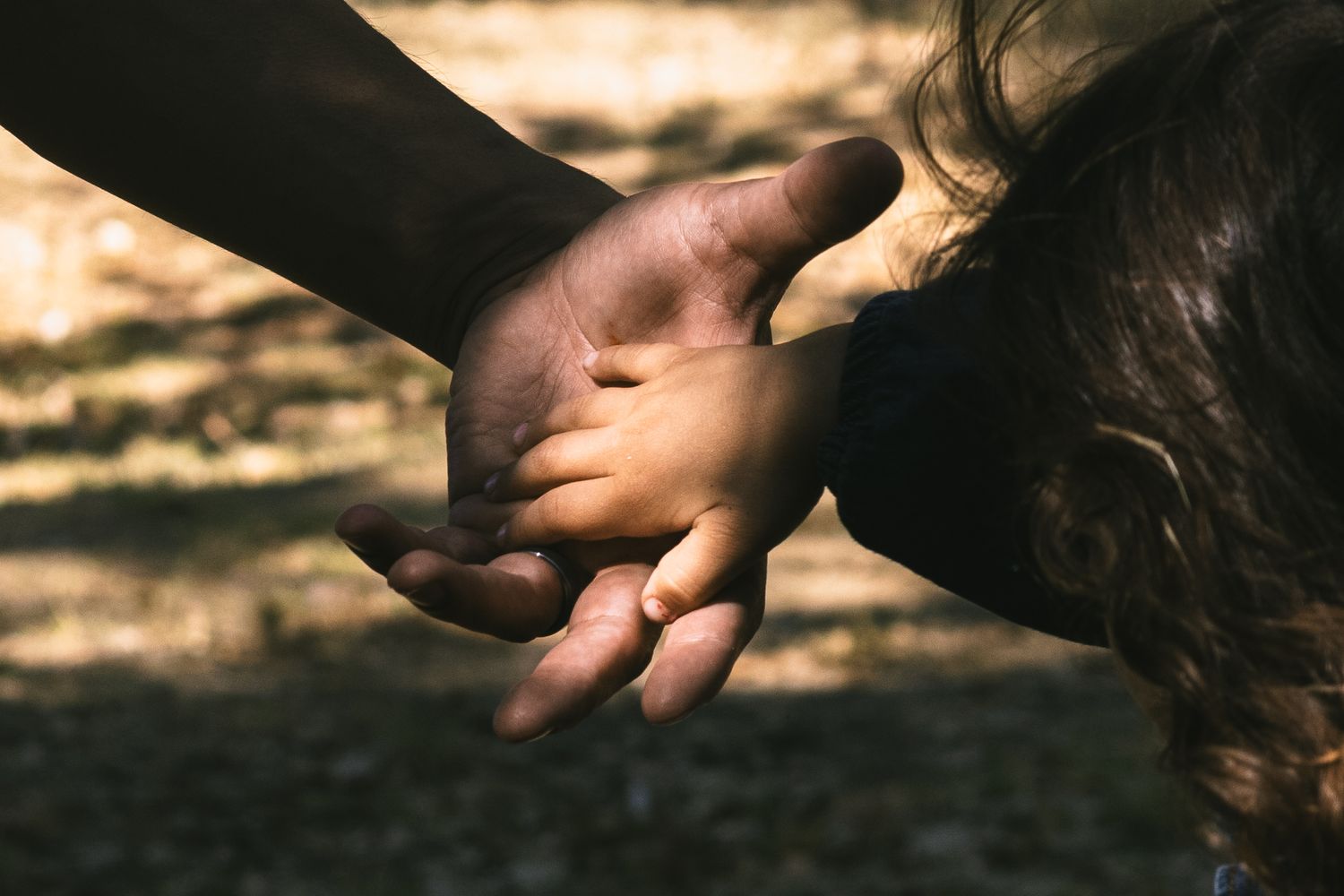 A close-up shot of two hands gently touching in a soft, natural outdoor lighting.