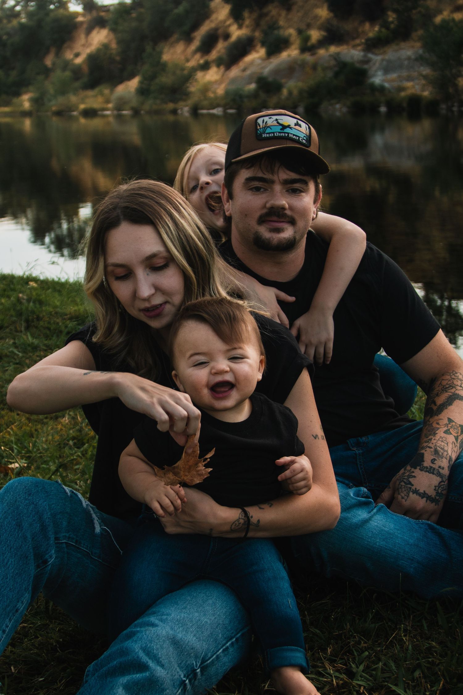 Family enjoying quality time together while relaxing on grass near a lake.