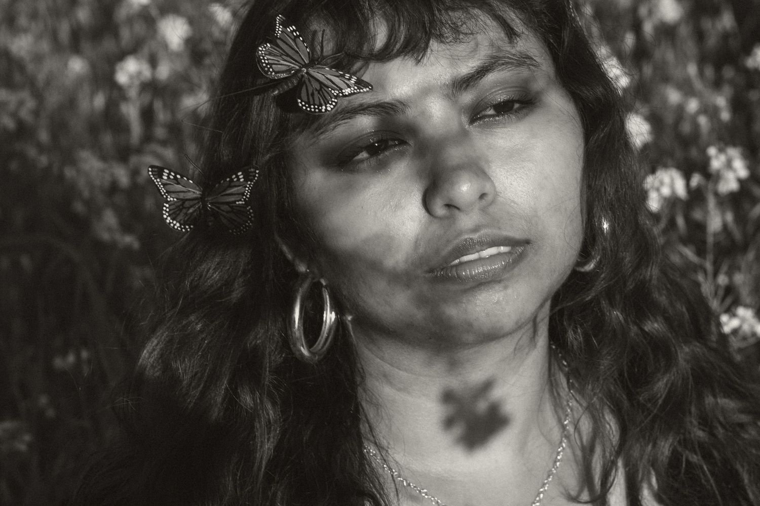Black and white portrait of someone with long curly hair wearing silver hoop earrings and delicate butterfly hair clips.