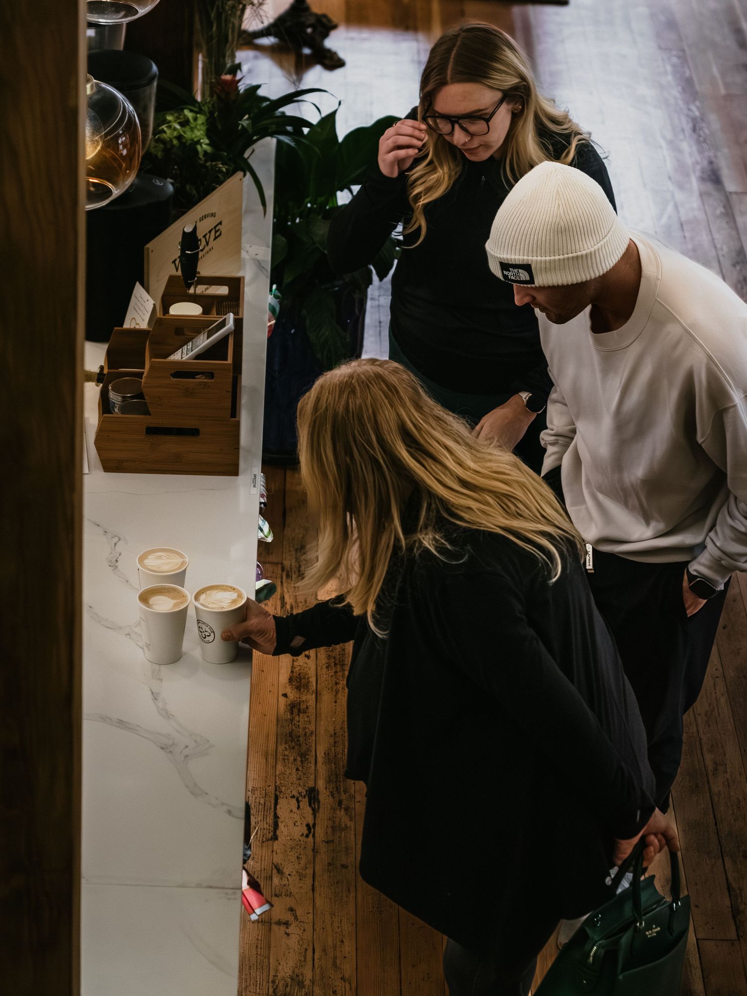 Customers gathering around wooden tables in a bright modern coffee shop setting.