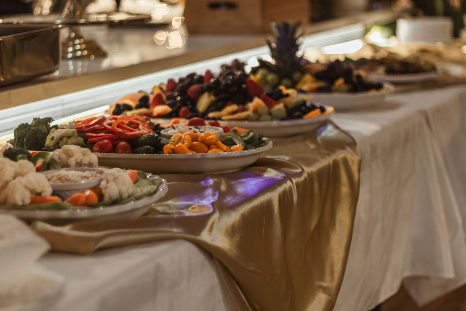 Elegant buffet table with colorful fresh fruit, vegetable platters, and gourmet appetizers at a catered event.