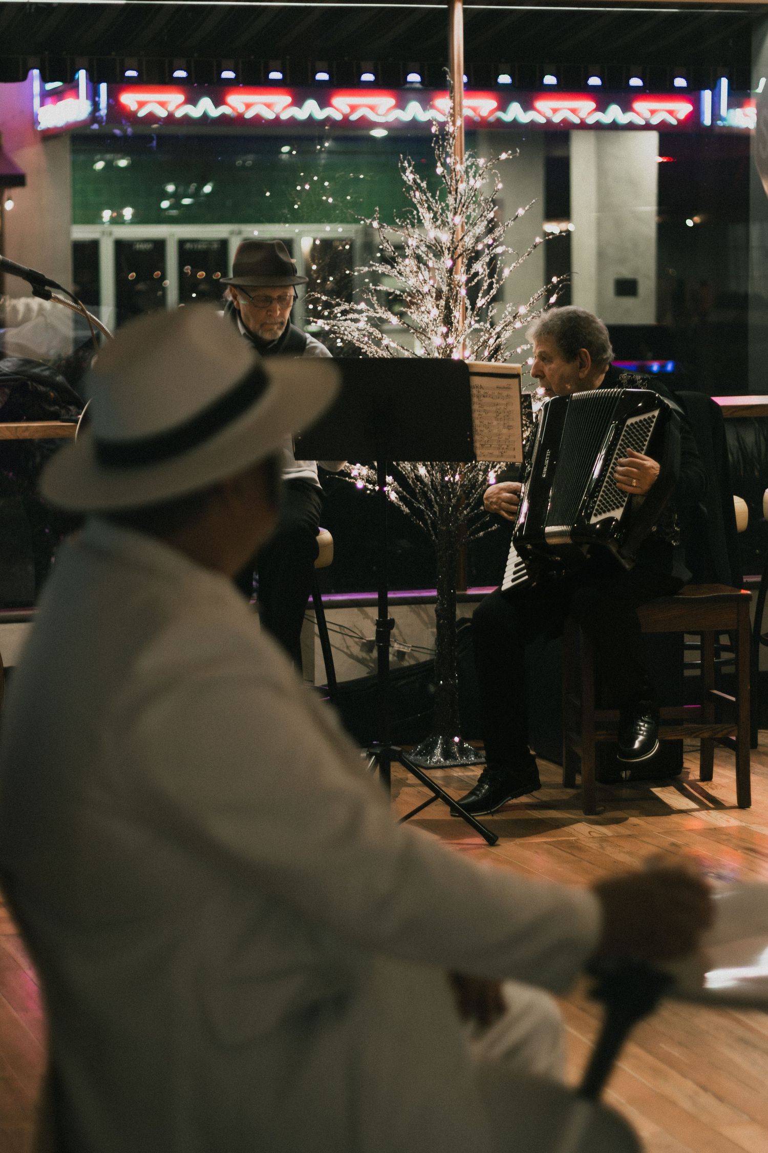 Musicians play accordion and read sheet music at a festive indoor evening event.
