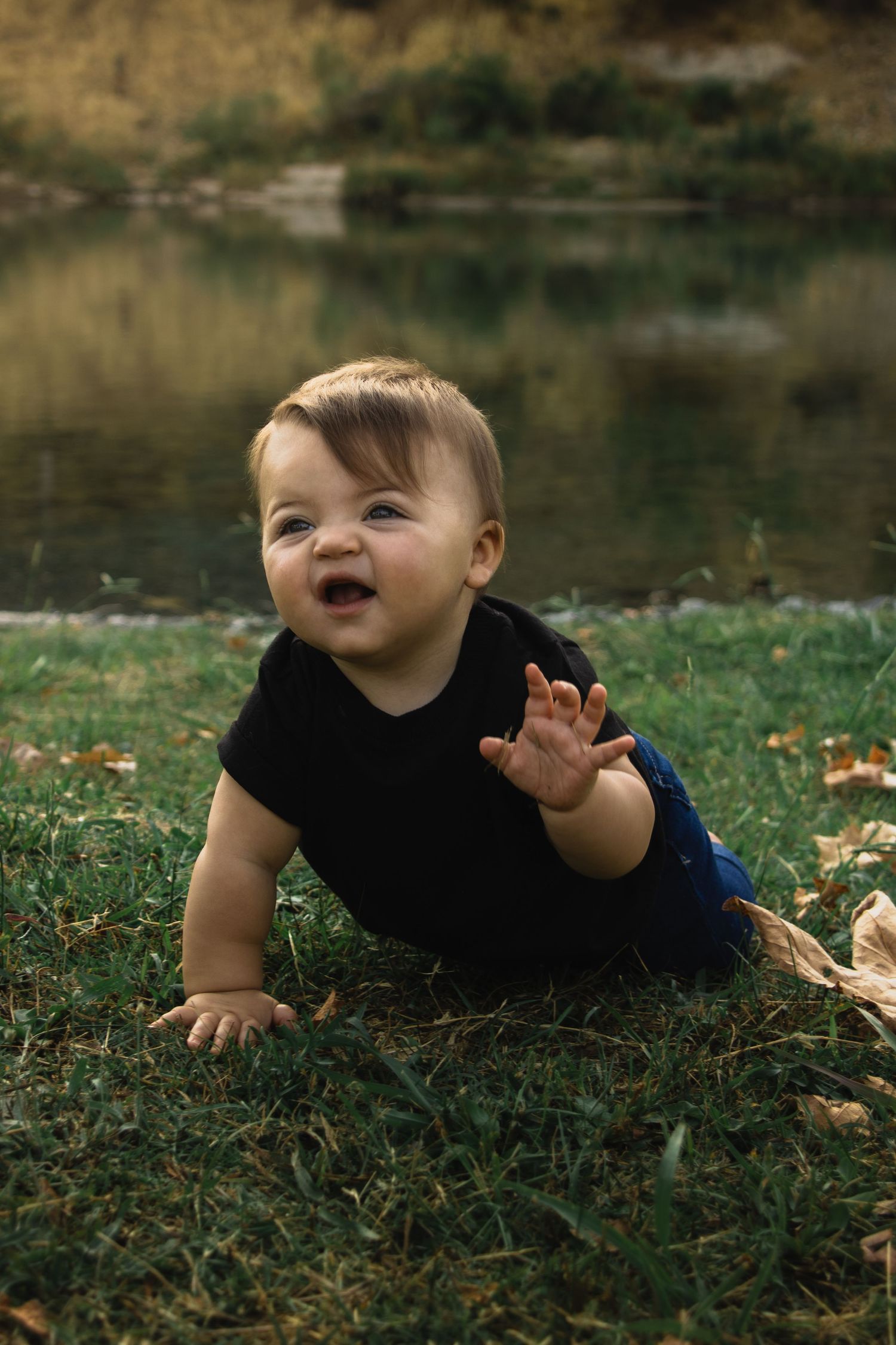 Baby in black outfit crawling on grass with fallen autumn leaves.