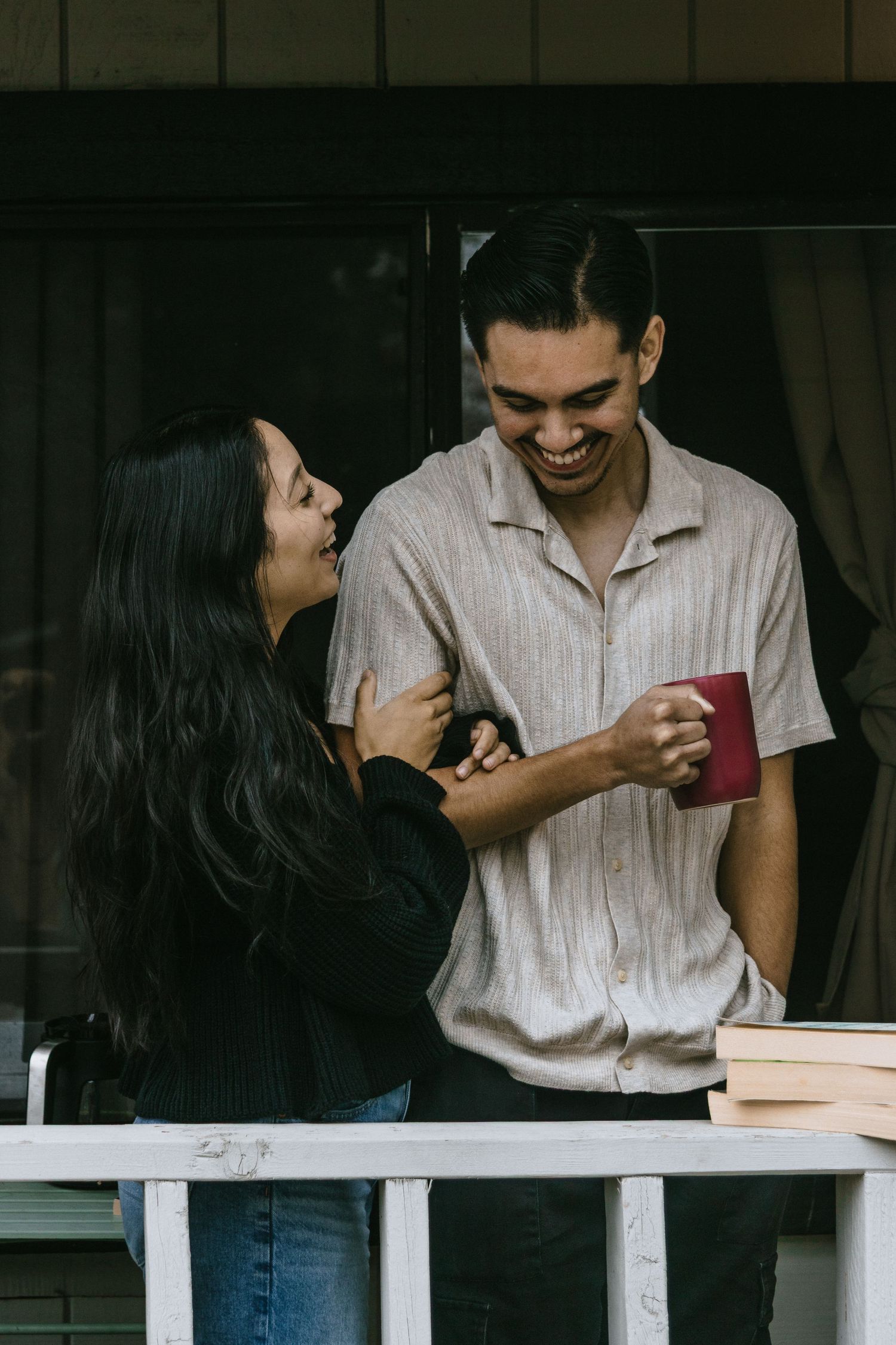 Couple sharing intimate conversation on white porch railing with coffee.