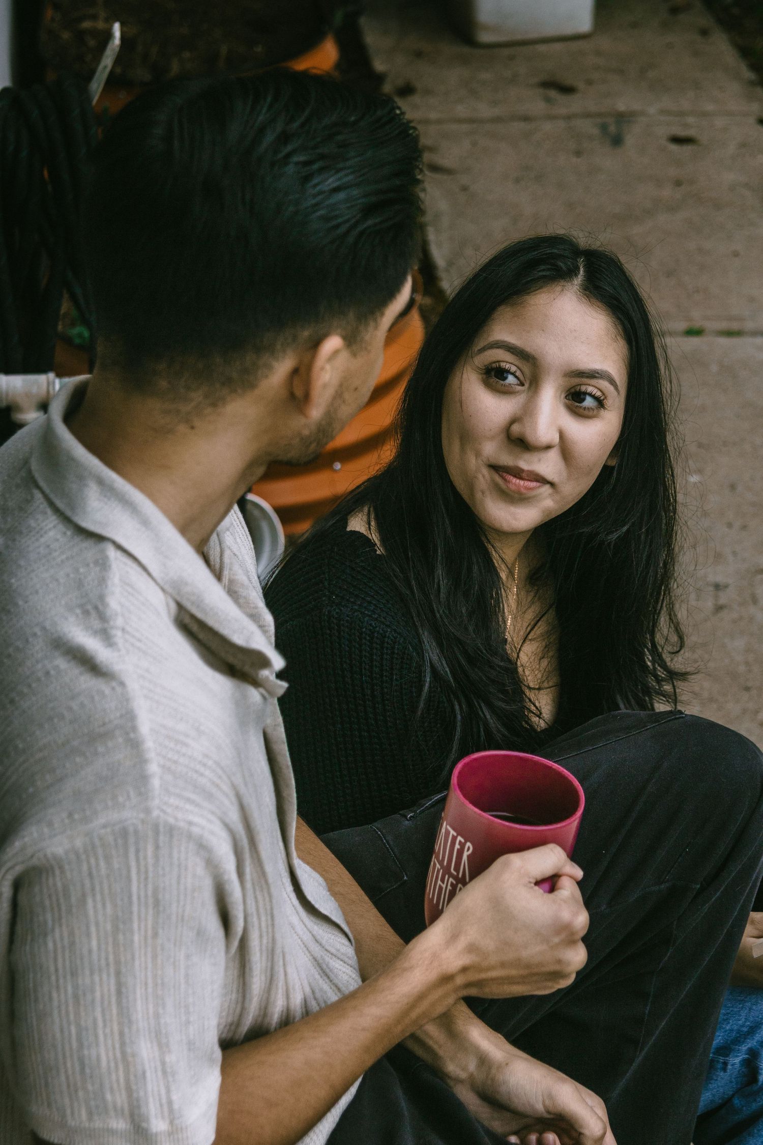 A couple shares an intimate moment over coffee in a dimly lit setting, with one person holding a burgundy mug.