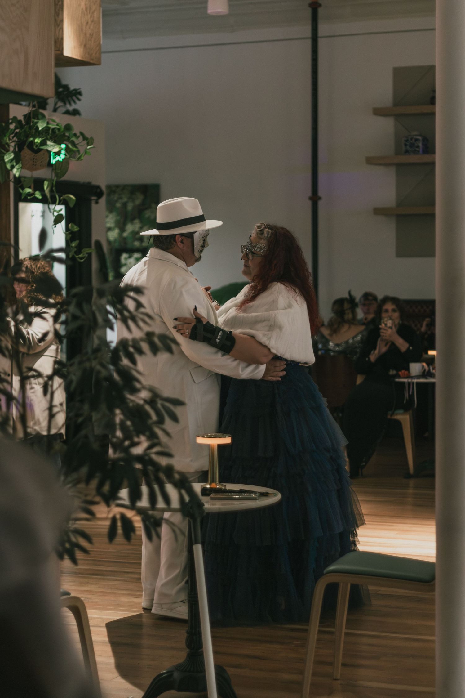 An elegant couple dances together in a warmly lit restaurant while guests watch.