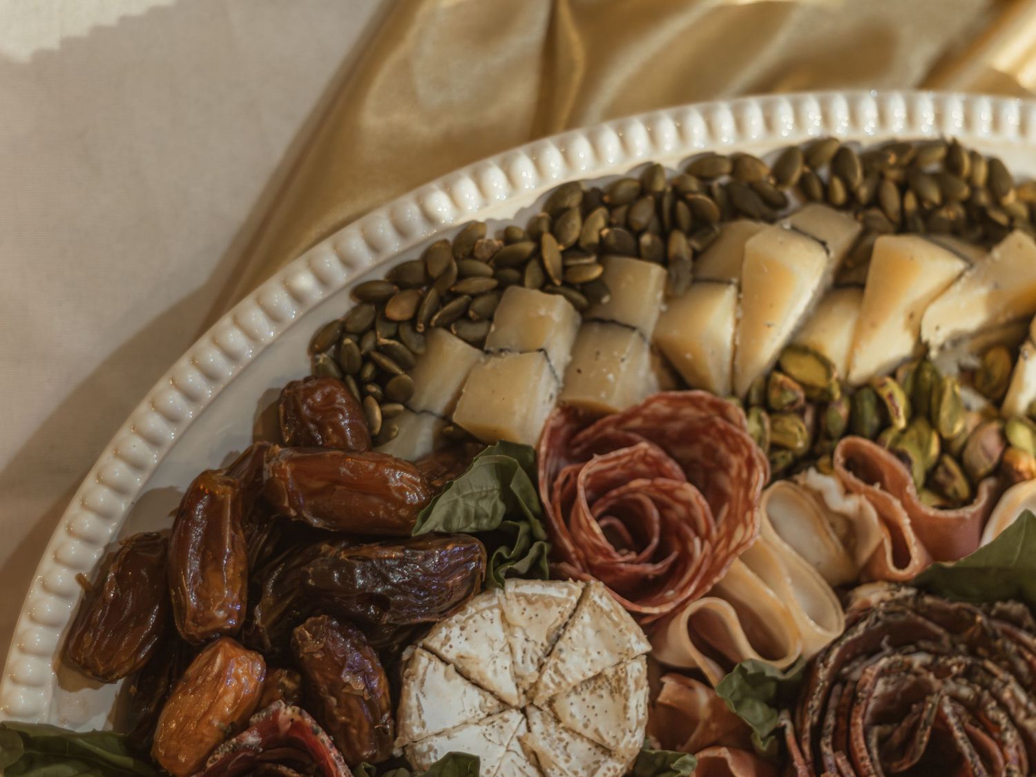Close-up view of a gourmet platter with dried dates, baklava pastries, and decorative rose-shaped garnishes on a white plate.