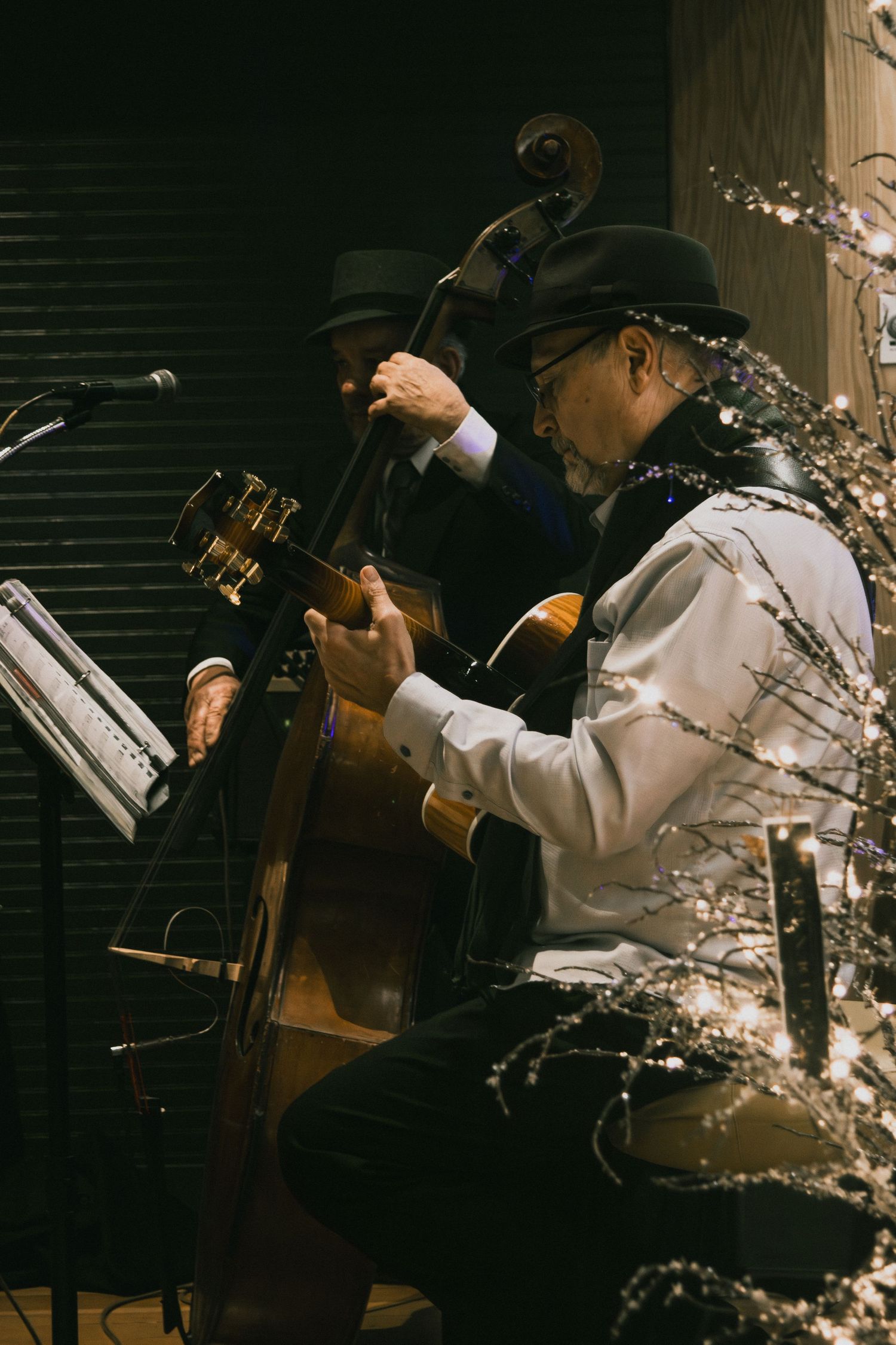 Two musicians perform jazz, one playing acoustic guitar and another upright bass, beside white floral decor.