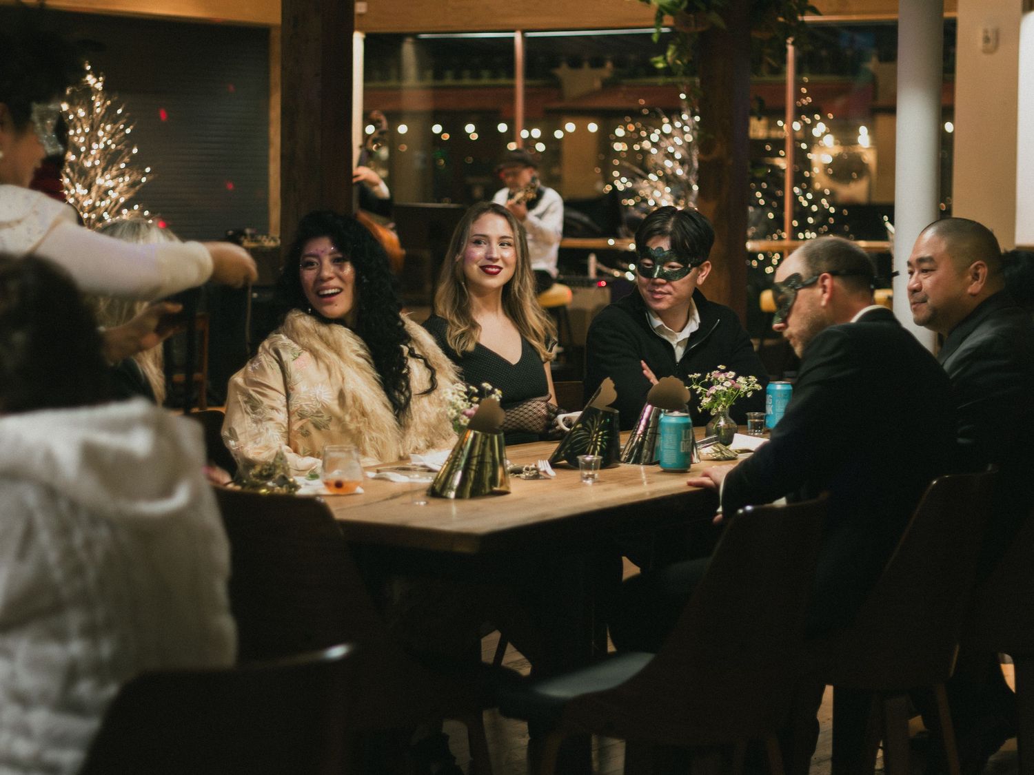 Group of friends enjoying a festive holiday dinner party at a warmly lit restaurant with Christmas tree decor.