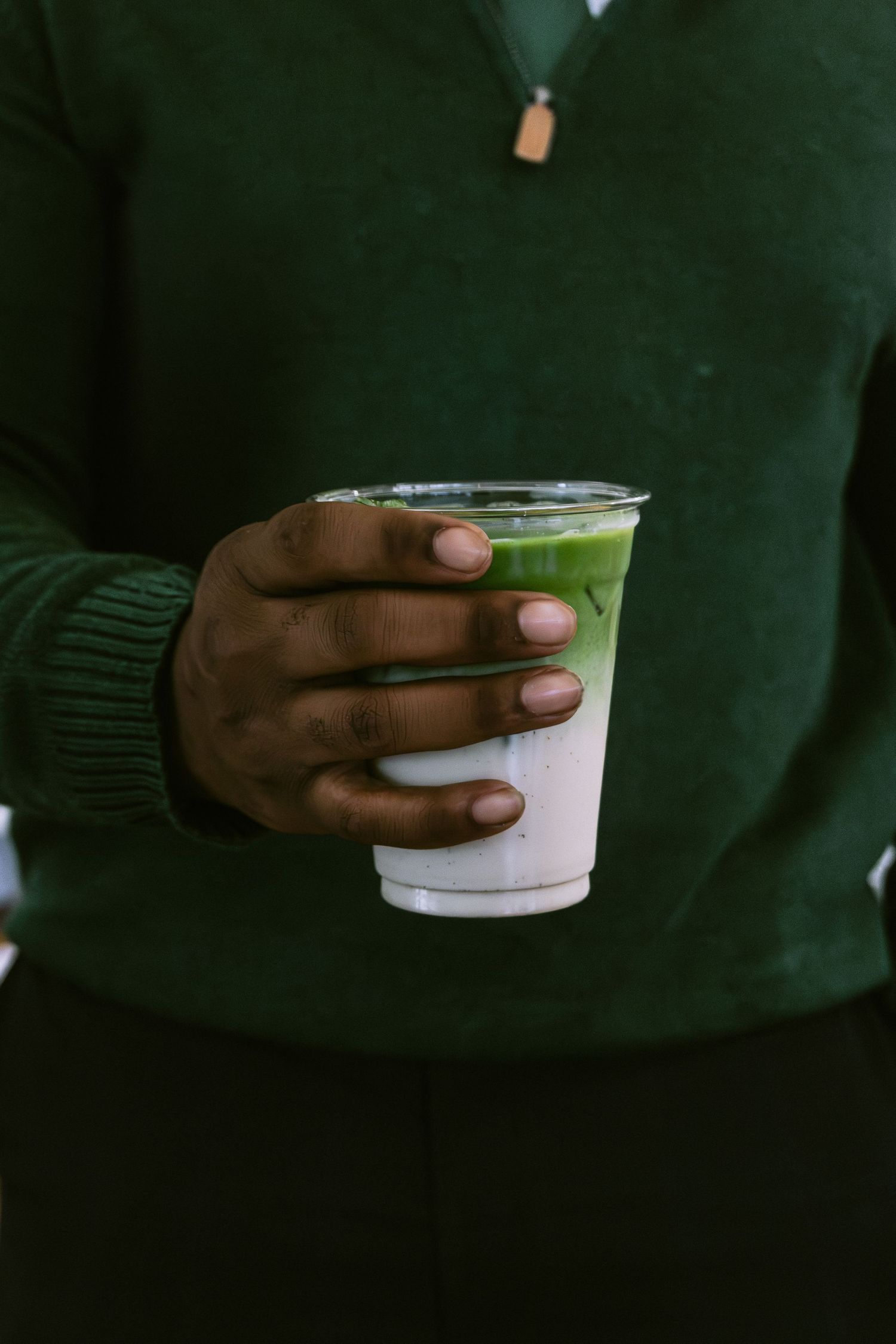 Hand holding a layered ombre green beverage in clear plastic cup.
