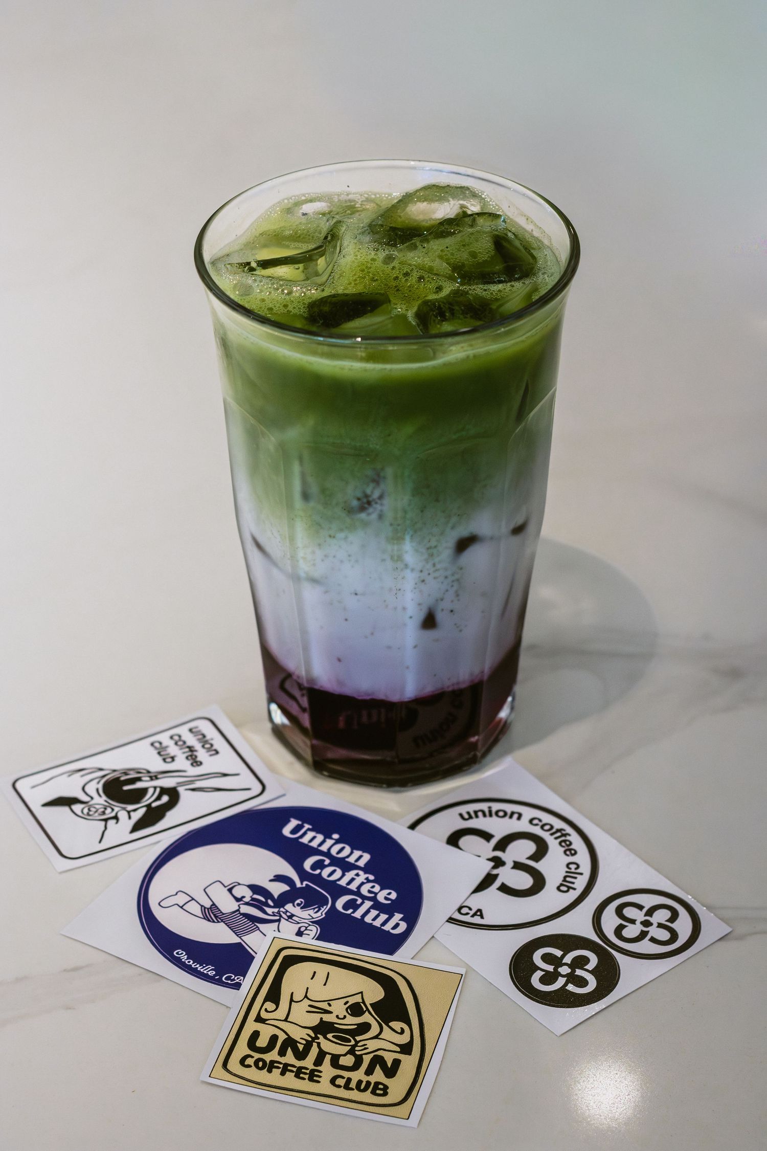 Layered green matcha latte with coffee shop stickers displayed on a white surface.