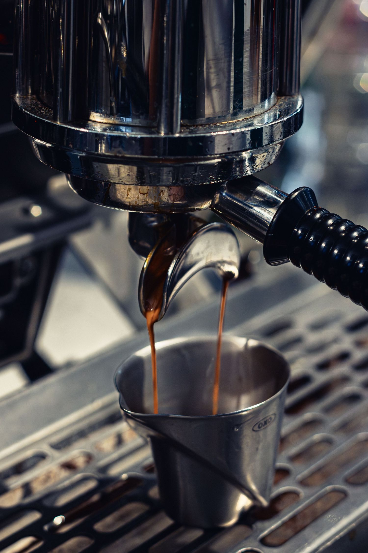 Fresh espresso pouring from a commercial coffee machine into a metal cup.