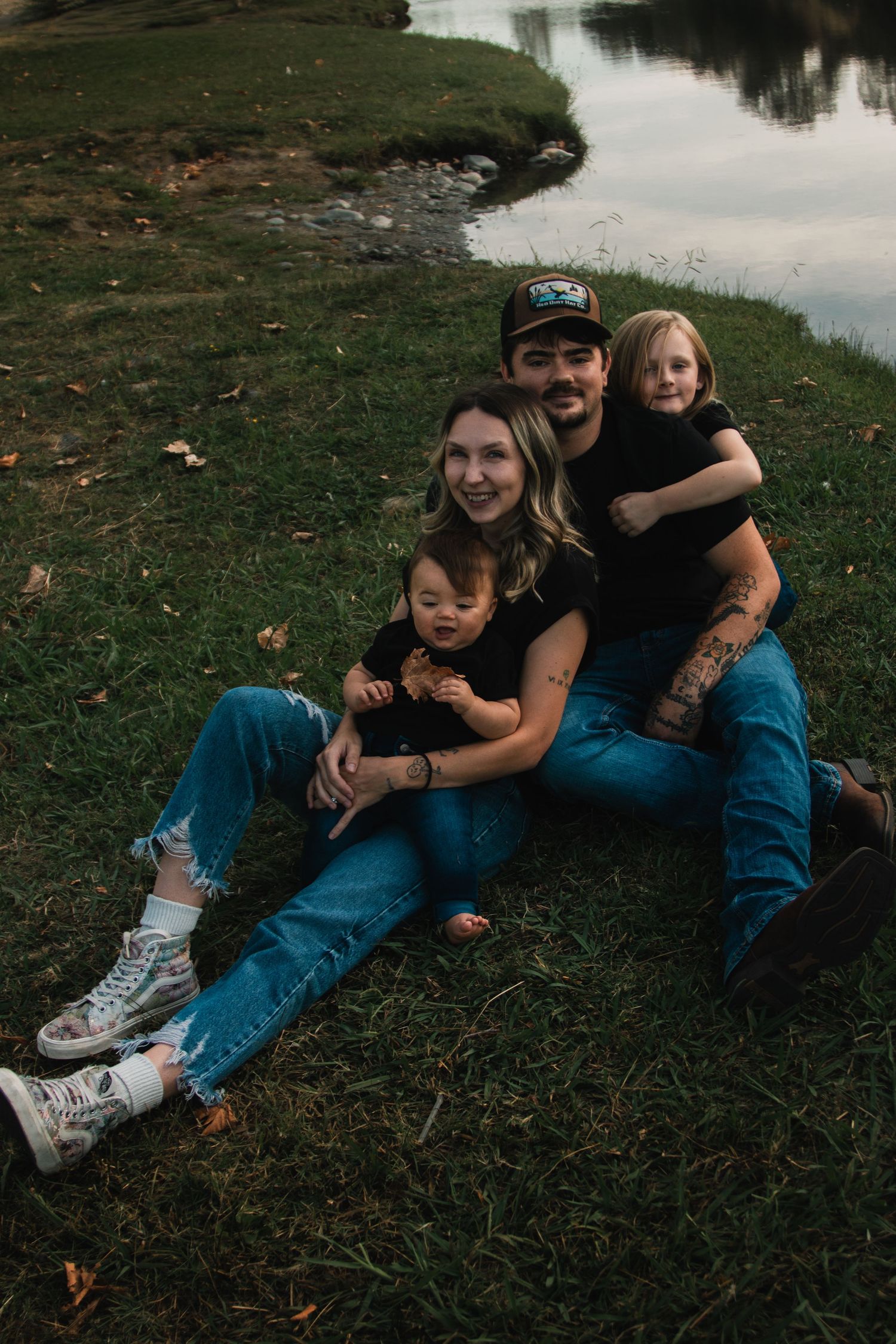 Family members lounging together on grass by a serene lake during golden hour.